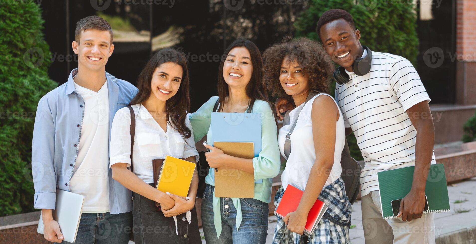 Portrait of happy international students posing outdoors near university building, smiling and embracing, taking group photo, panorama photo
