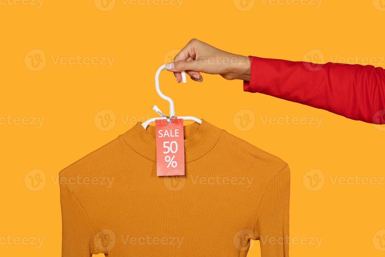 This image shows a hand holding a yellow mock-up sweater on a hanger. The sweater has 50 percent off sale tag attached to it. The background is a bright yellow color, cropped photo