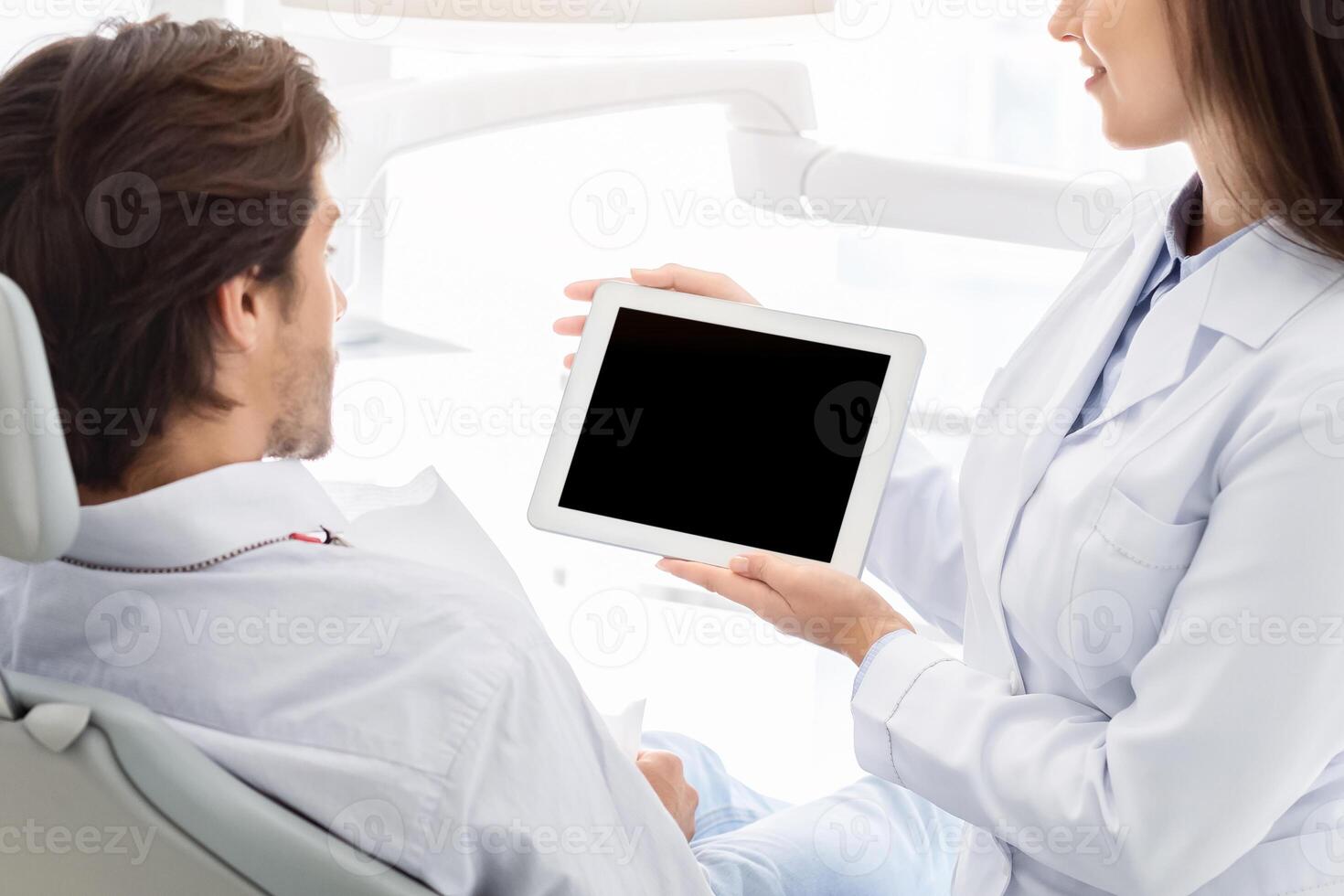 Female dentist showing male patient empty digital tablet screen, modern technologies in stomatology, copy space photo