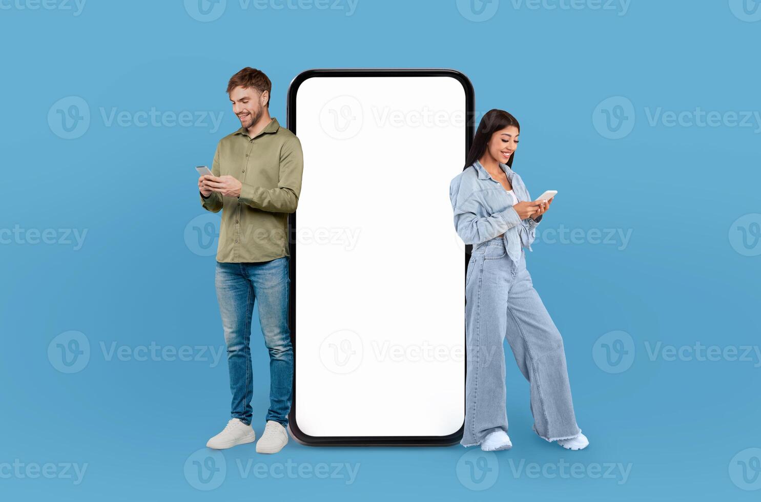 A man and woman are positioned beside a blank screen on a blue background. Both individuals are looking towards the screen in a professional setting. photo