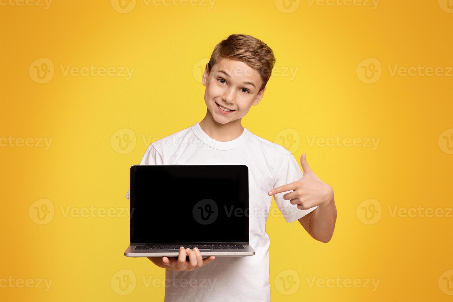 Smiling teenager boy pointing at blank screen of laptop, recommend educational website or application, mockup photo