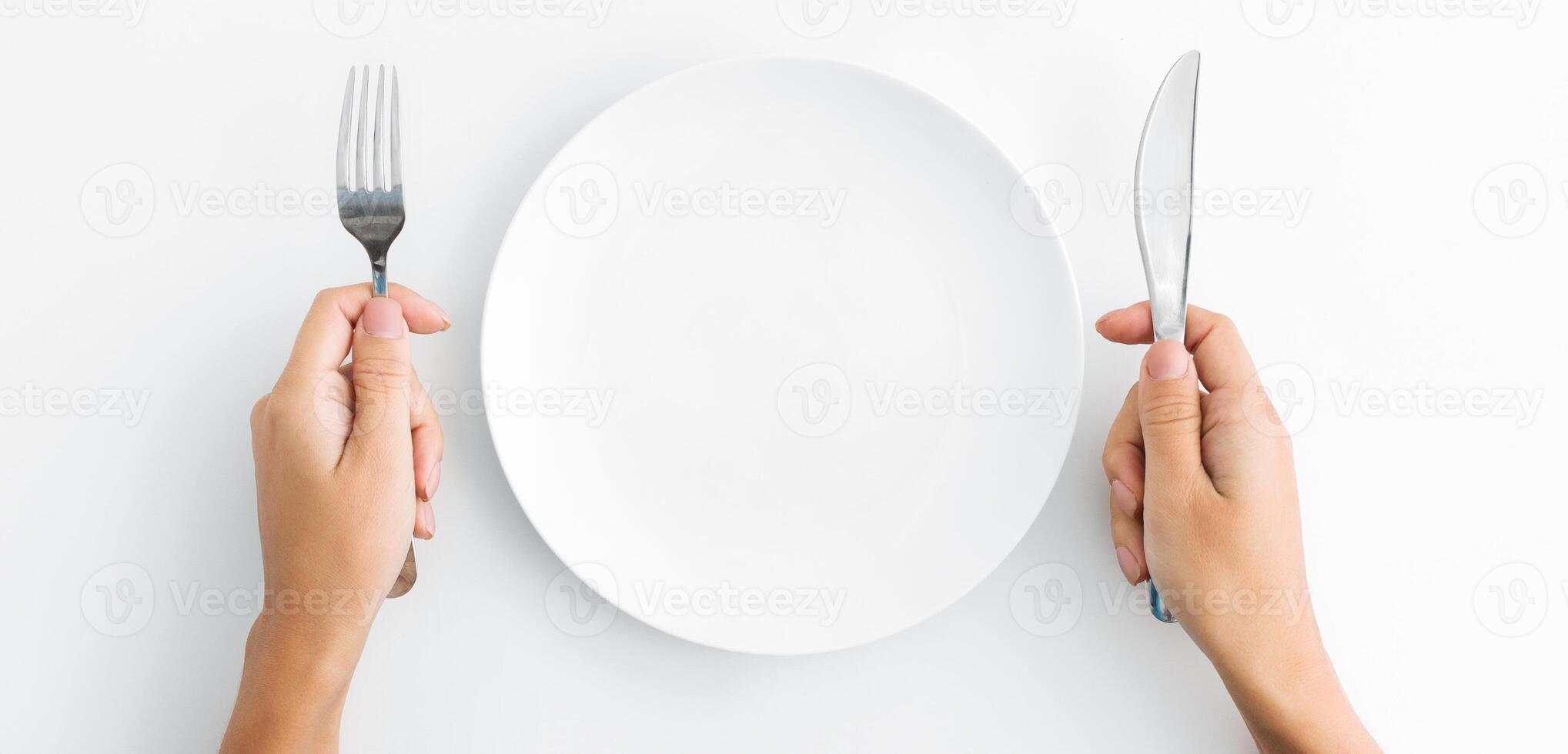 Dinner place setting. White empty plate and hand holding silver fork and spoon on white background, top view, copy space photo