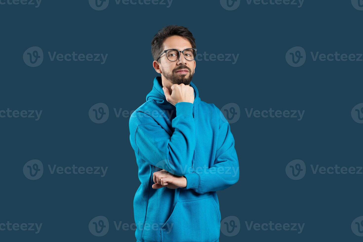 A man wearing glasses and a blue jacket is standing in the image. He has a serious expression on his face and seems to be looking straight ahead photo