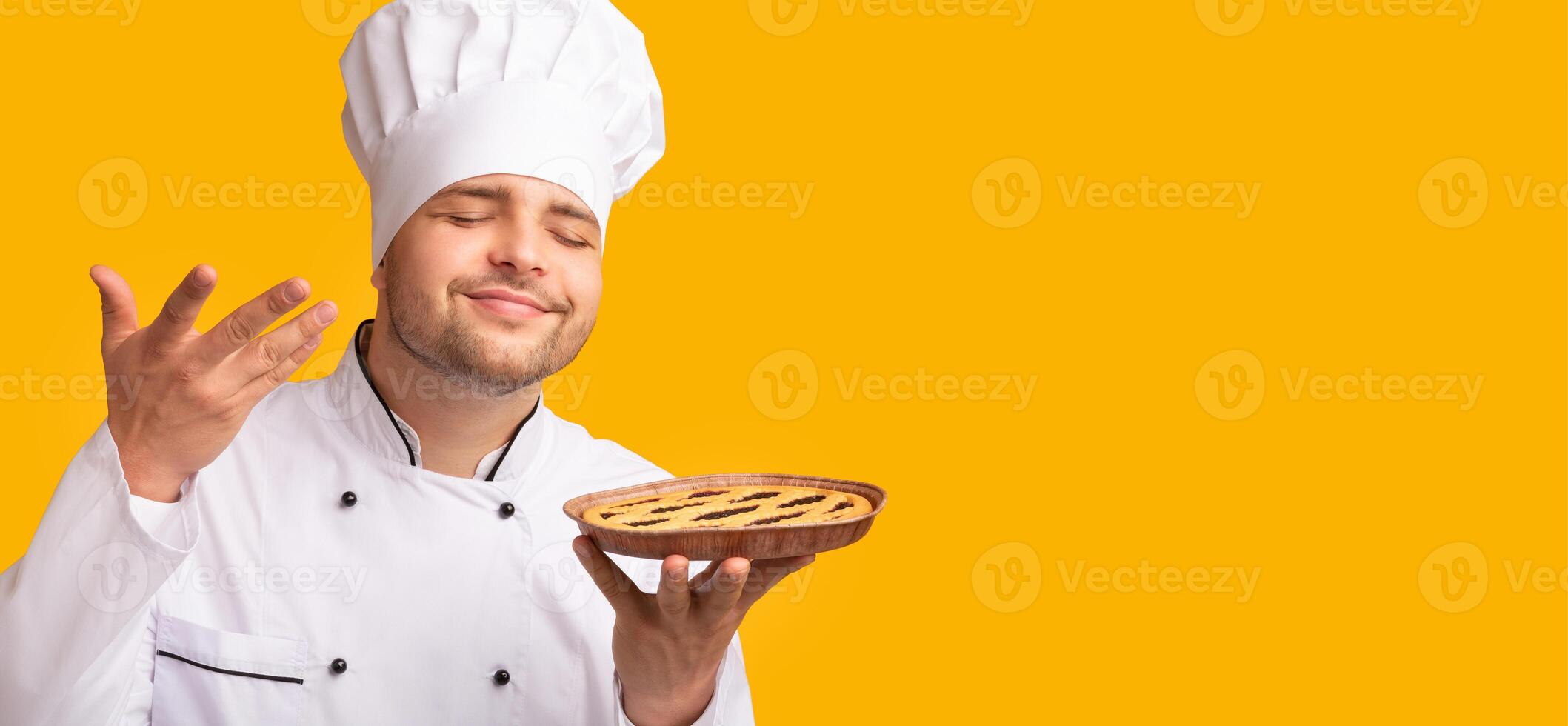 Smiling Baker Guy Smelling Baked Pie Standing Over Yellow Background. Culinary Recipes Concept. Studio Shot photo