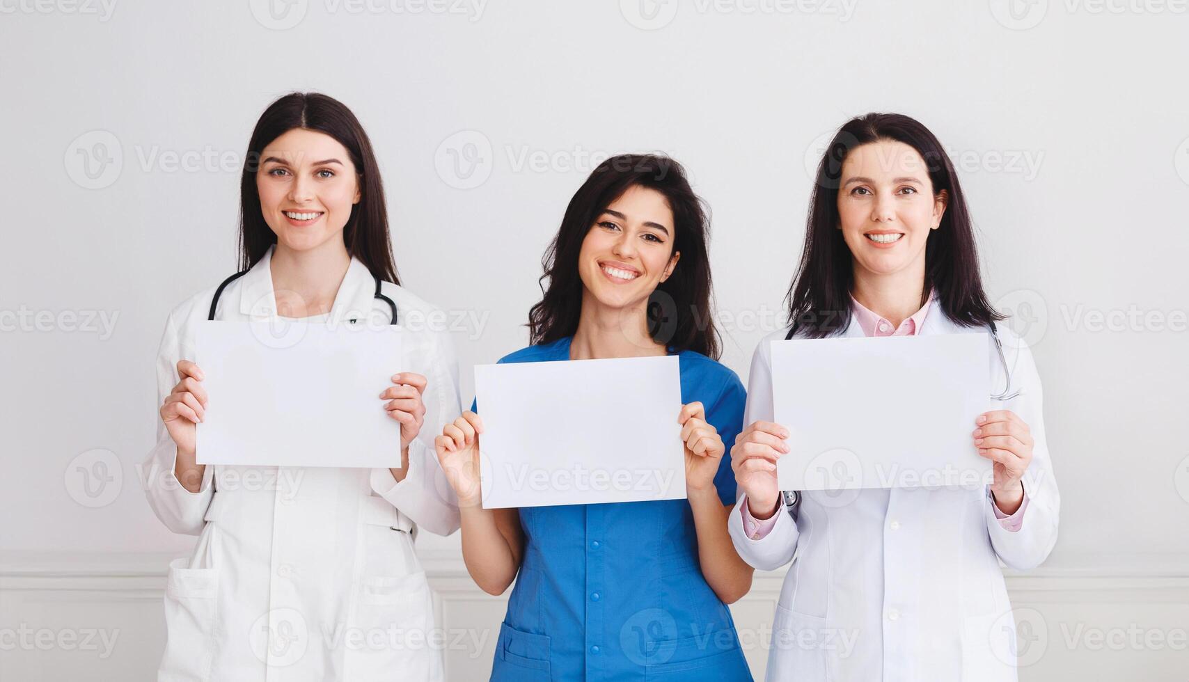 Medical Information. Doctors And Interns Holding Empty Papers, Standing In Hospital Over Grey Wall photo