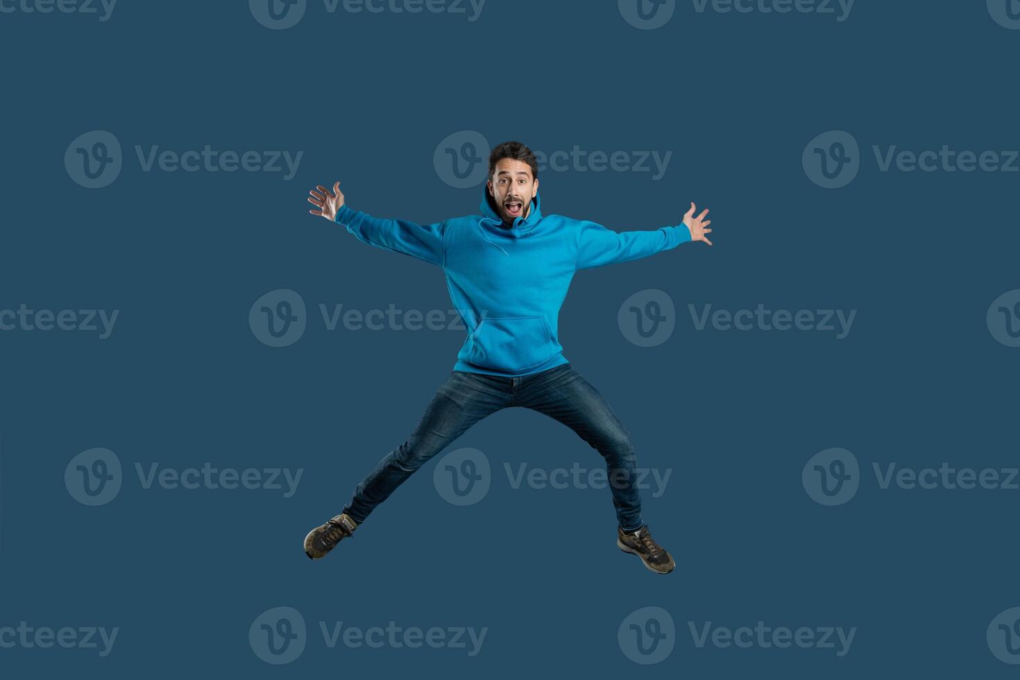 A man wearing a blue shirt is captured mid-air as he jumps energetically. His body is stretched upwards with his arms raised, showcasing a moment of dynamic movement. photo