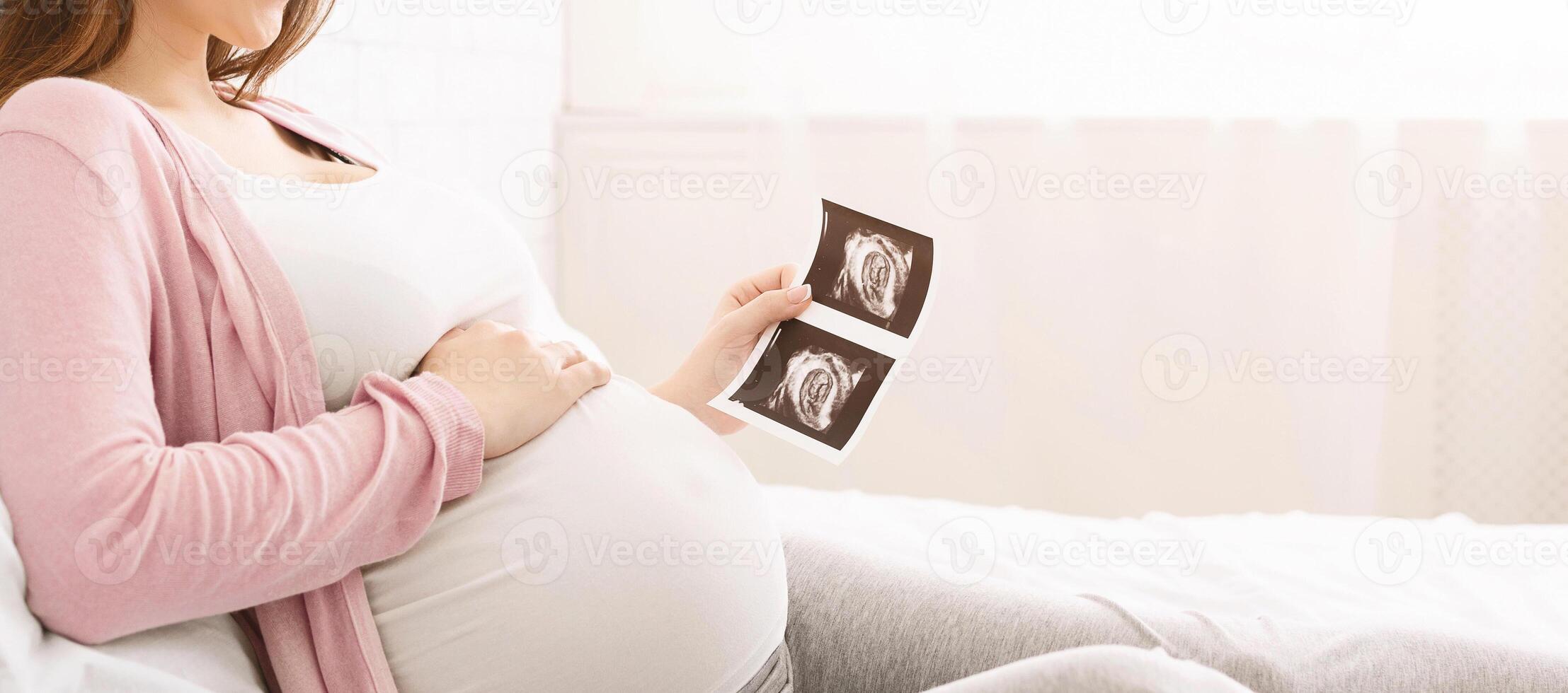 Concept of pregnancy and health care. Young mother waiting for baby, enjoying sonogram in bed, panorama with empty space photo