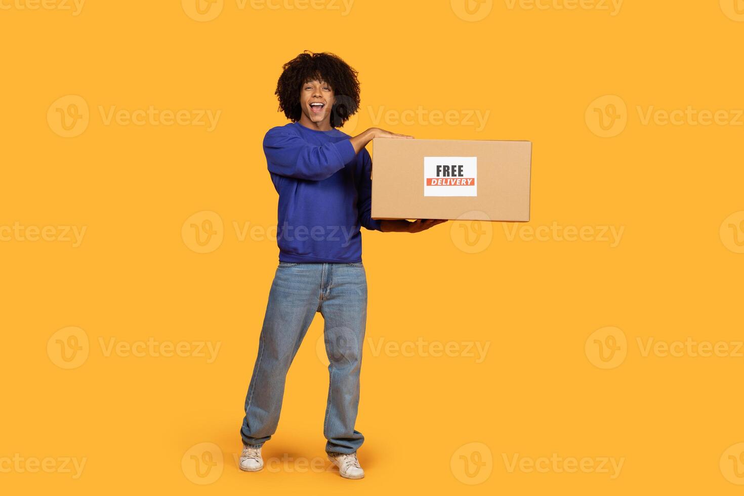 A man is standing and holding a box, which has a free delivery sign on it. He seems to be ready to deliver the package to a customer. photo