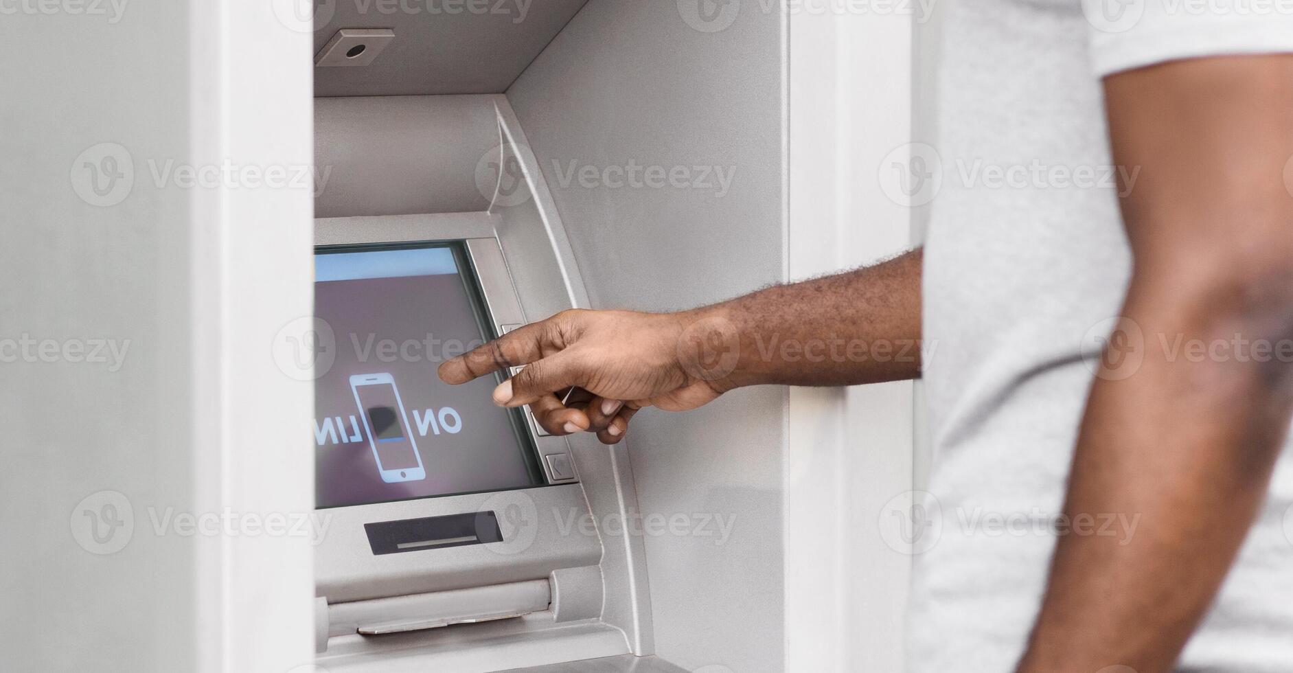 A man uses an ATM machine, pointing his finger at the screen. photo