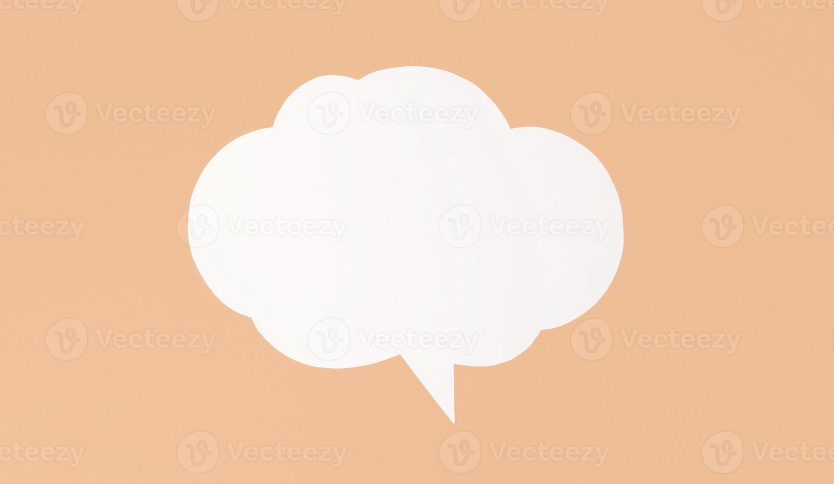 White paper speech bubble sits on peach background. The bubble is shaped like cloud and has single tail pointing downwards. It is a simple, clean image that could be used for a variety of purposes photo