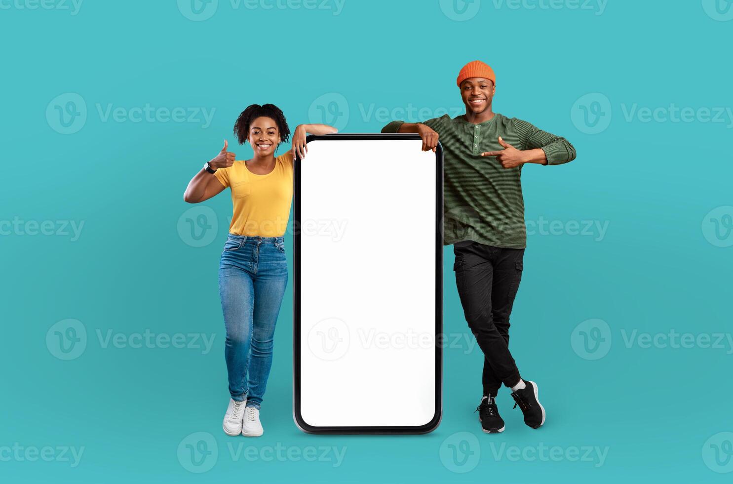 A young Black man and woman are standing together, holding up a blank phone screen. They are looking at the screen with focused expressions, possibly sharing information or taking a photo. photo