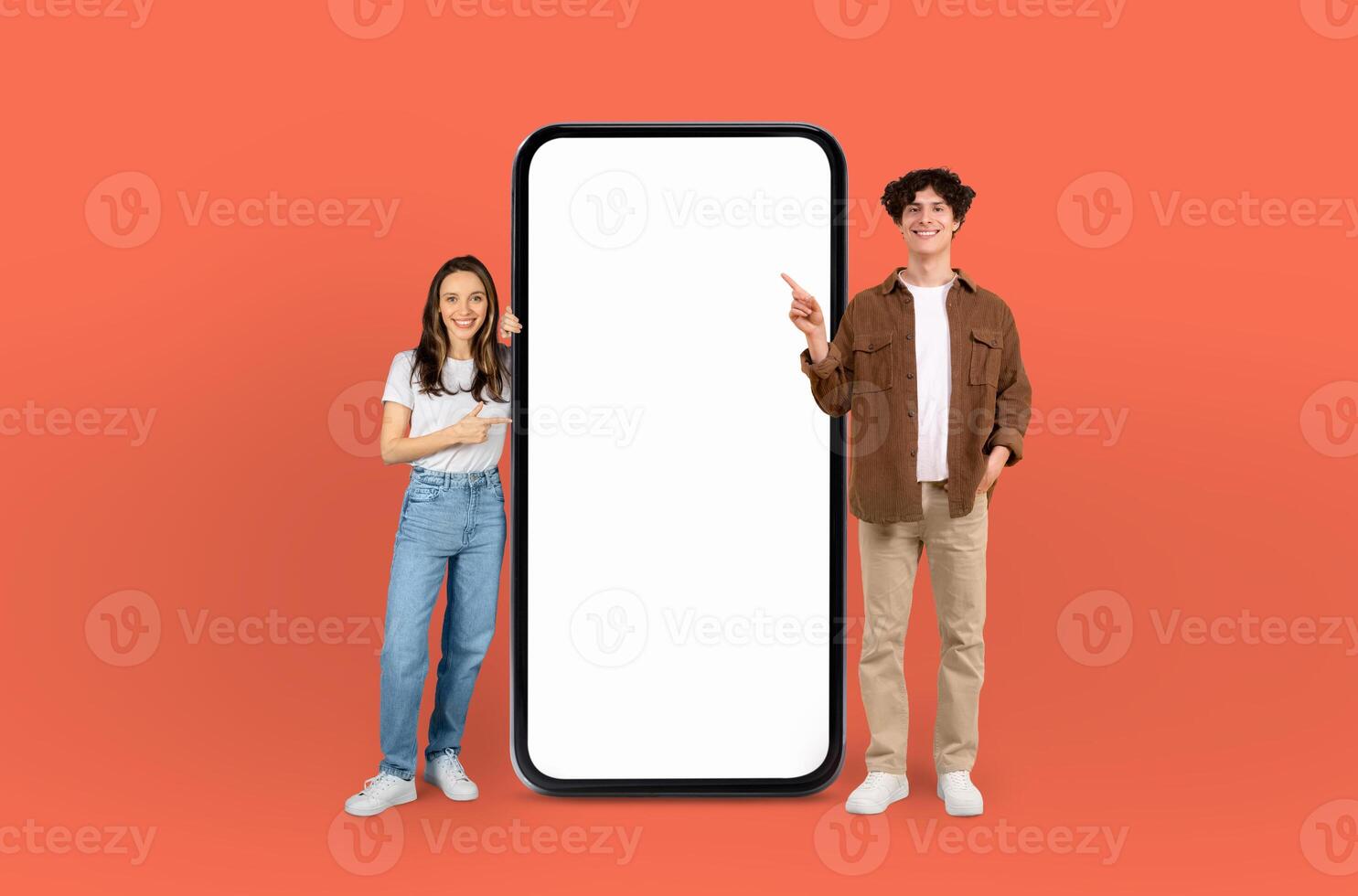 A man and woman are standing in front of a blank screen, both pointing towards it, against a vibrant orange background. They seem to be discussing or presenting something on the screen. photo