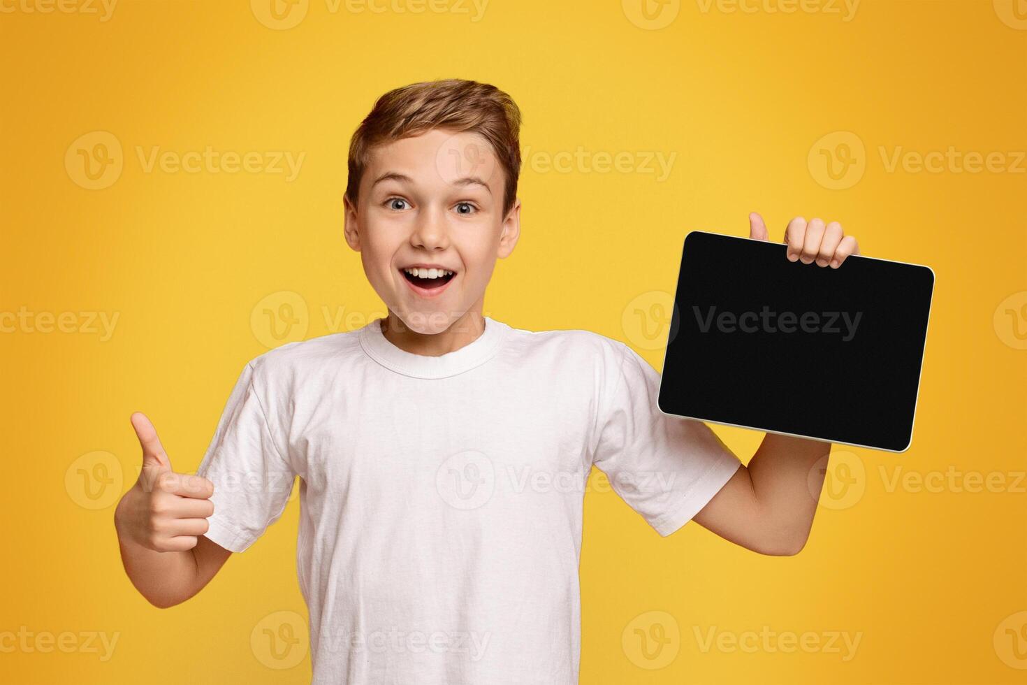 Awesome application or website. Excited teenage boy showing blank digital tablet screen and gesturing thumb up, orange background, free space photo