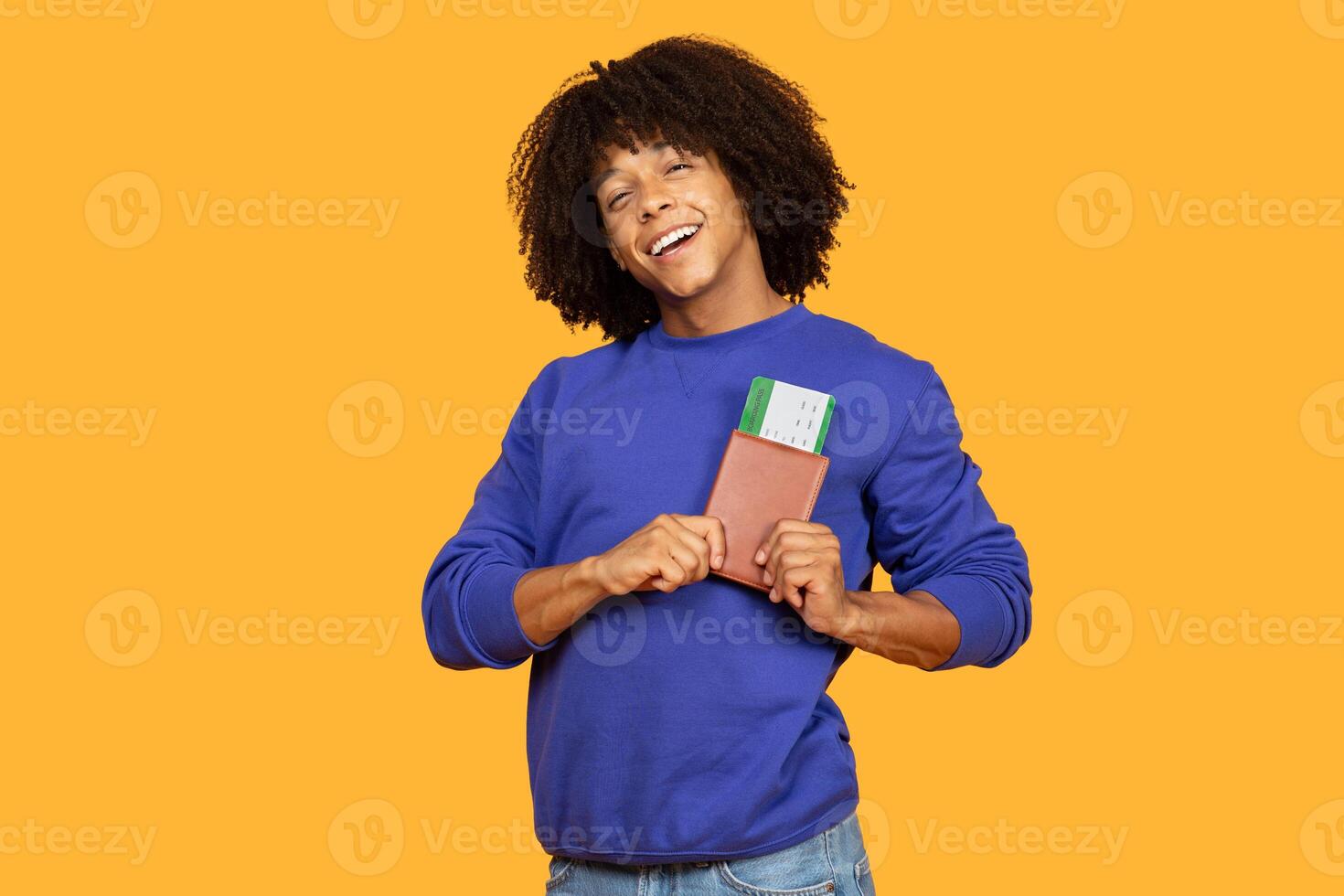 A joyful young man in a blue sweater stands against a vibrant yellow background, holding his passport and flight tickets, ready for his upcoming trip. photo