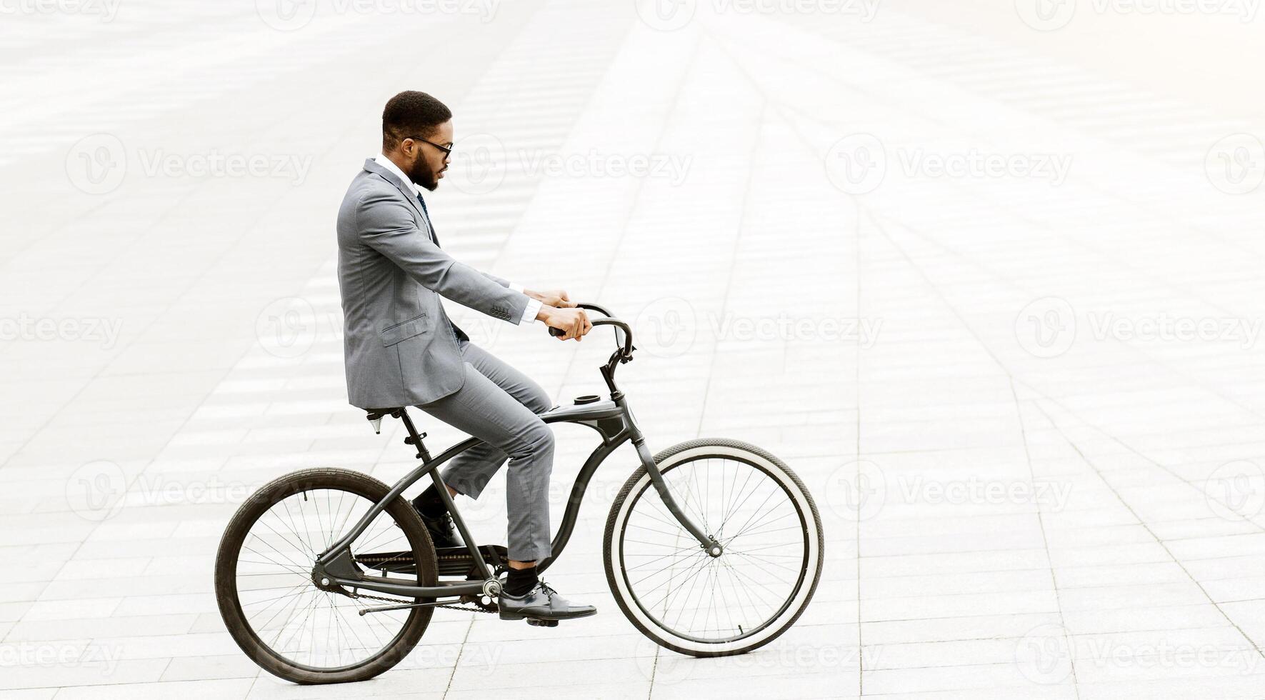 An African American professional is cycling through the city. The setting is urban and busy, highlighting the blend of business efficiency and active commuting. photo