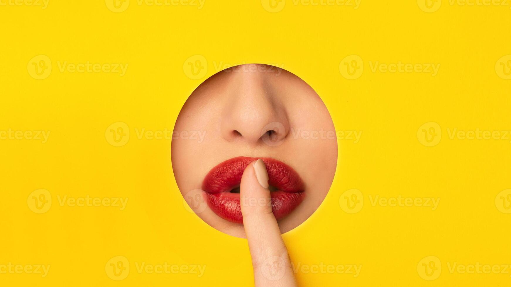 A close-up view of a woman gently touching her red lips on a bright yellow background. The contrast between the colorful backdrop and the soft texture of the lips creates a simple yet impactful image. photo