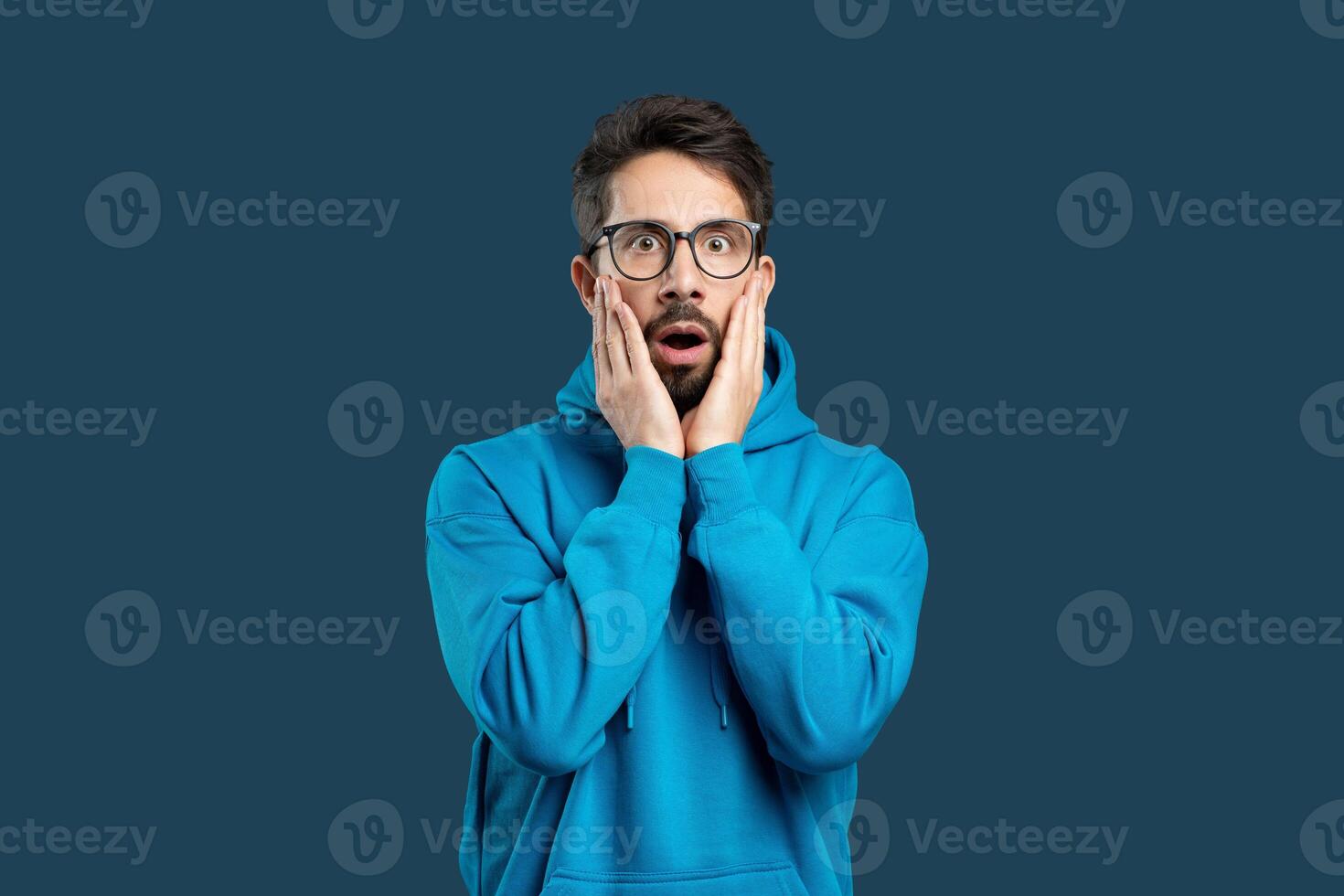 A man wearing a blue hoodie is covering his face with his hands in this candid street photograph. The mans expression is obscured, adding a sense of mystery to the scene. photo
