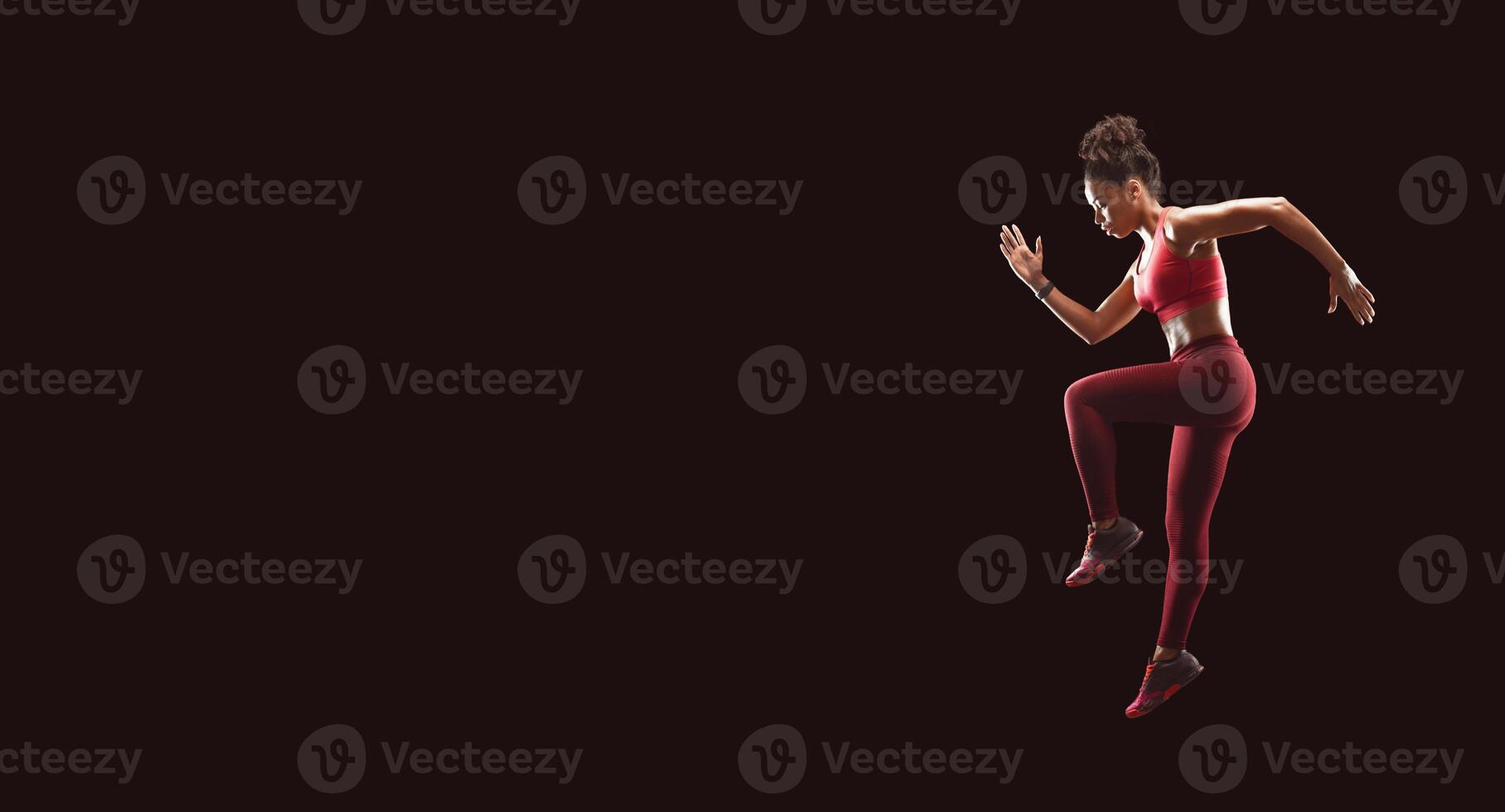 African fitness girl jumping, exercising over black background, side view photo