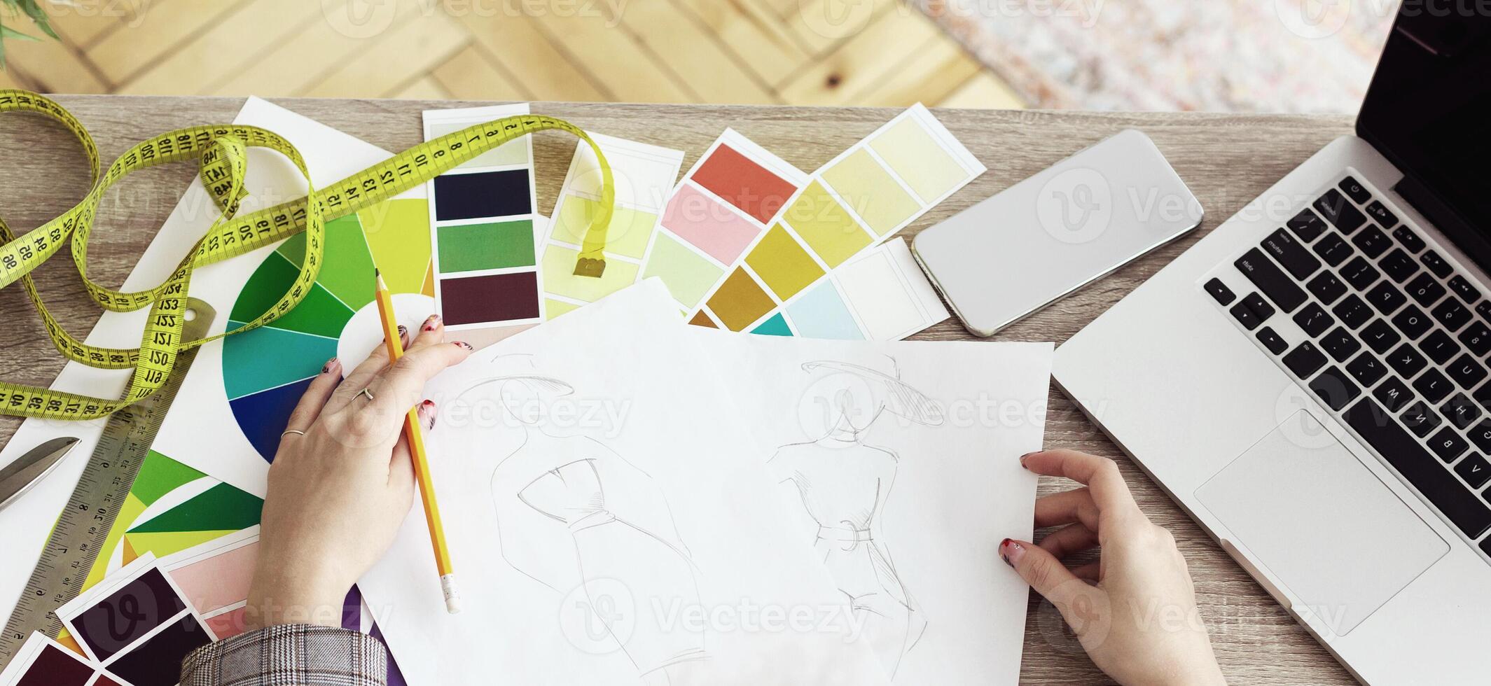 A fashion designer works on a sketch of a garment surrounded by tools, including color swatches, a tape measure, and a pencil. photo