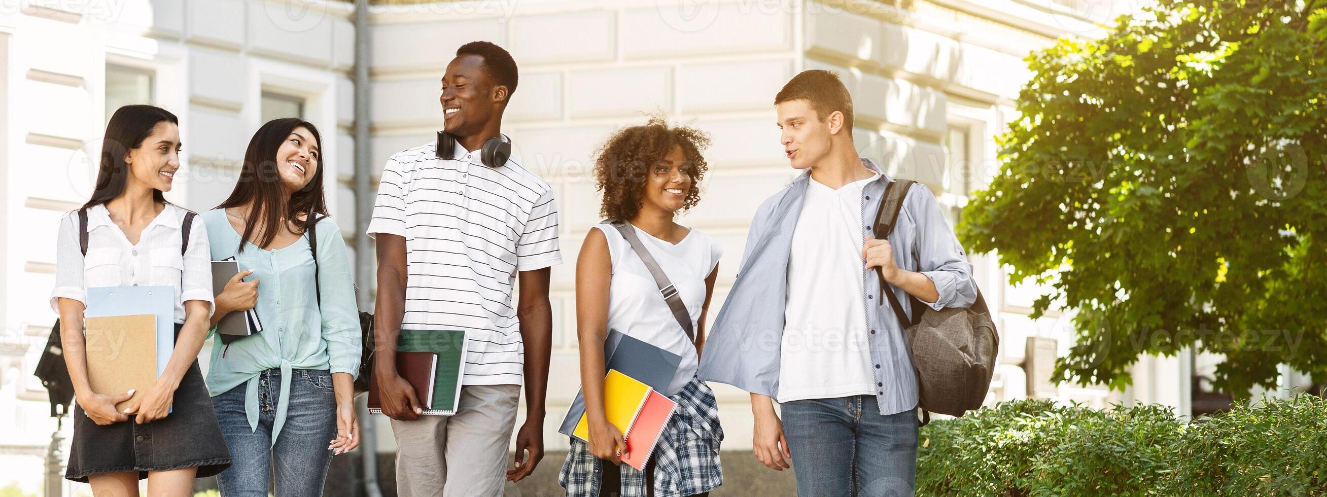 Campus Life. Group of international students walking outdoors after classes, holding workbooks, chatting together and smiling photo