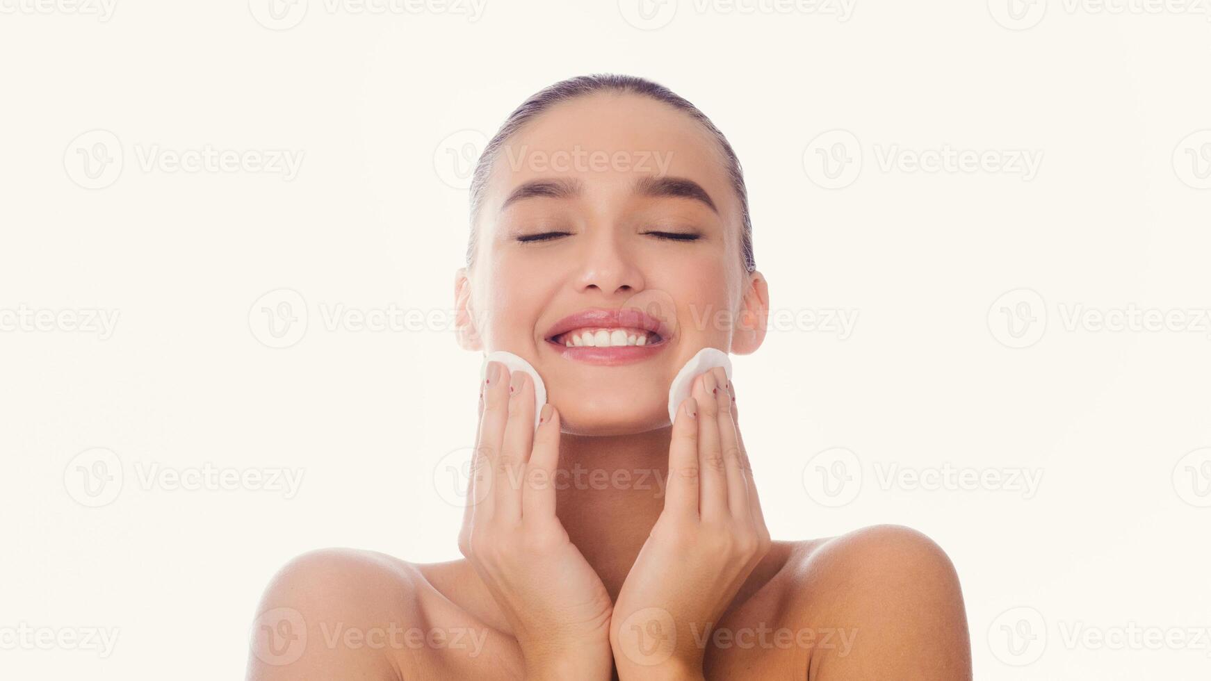 Happy woman is cleansing her face using a facial cleanser product. She is gently massaging the cleanser onto her skin to remove dirt and impurities. photo