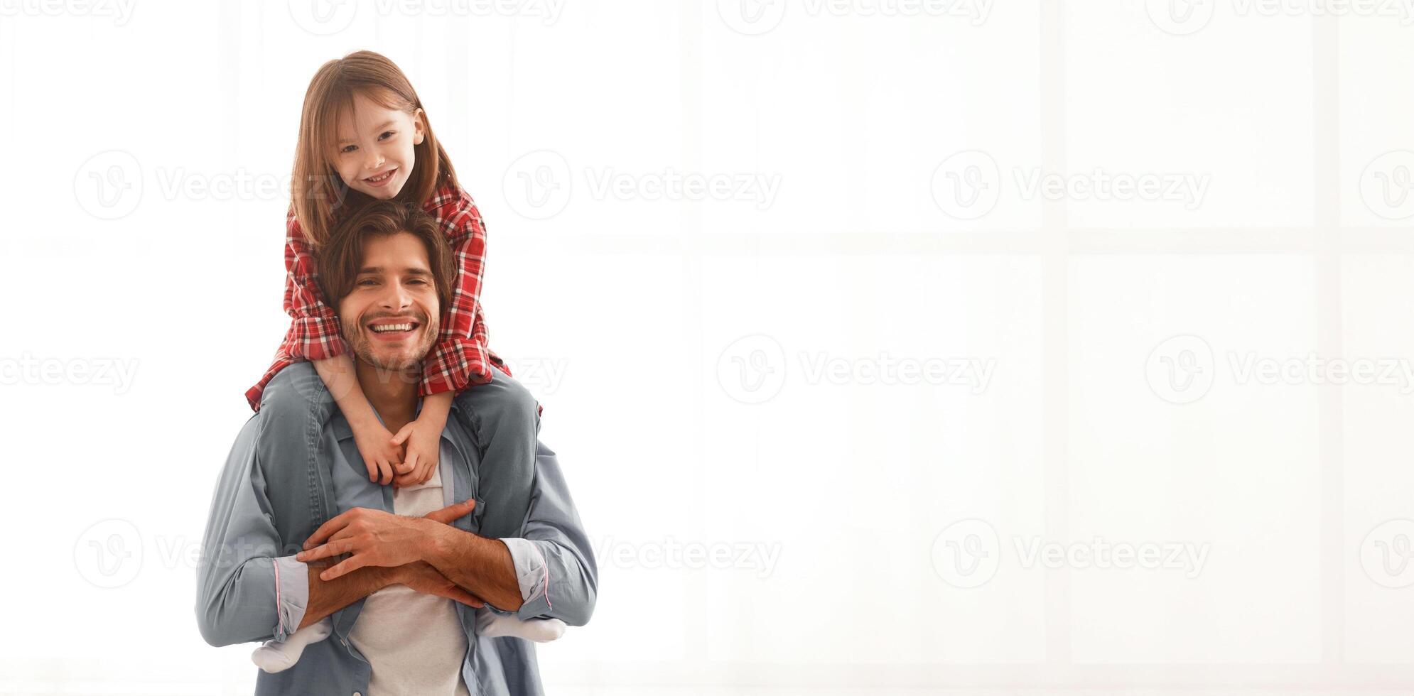 Smiling dad carrying his lovely cheerful little daughter on shoulders, having fun together at home, white background, free space photo