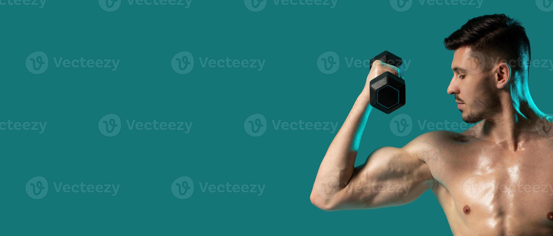 A man is lifting dumbbells while standing on a green background. He is focused and determined, with his muscles engaged, empty space photo