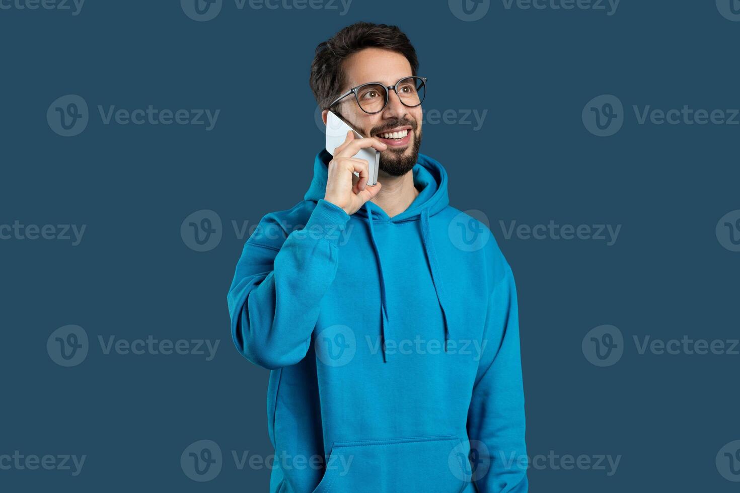 A man wearing a blue hoodie is engaged in a conversation on his cell phone. His attention is focused on the call as he stands in a public area. photo