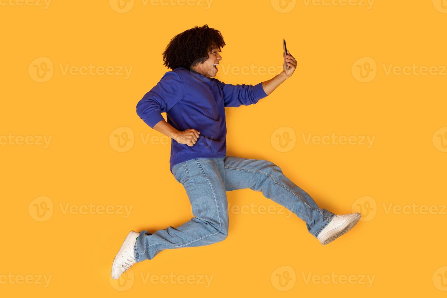 A man is mid-air, captured while jumping energetically with one hand holding a cell phone. His body is in motion, creating a dynamic and active scene. photo