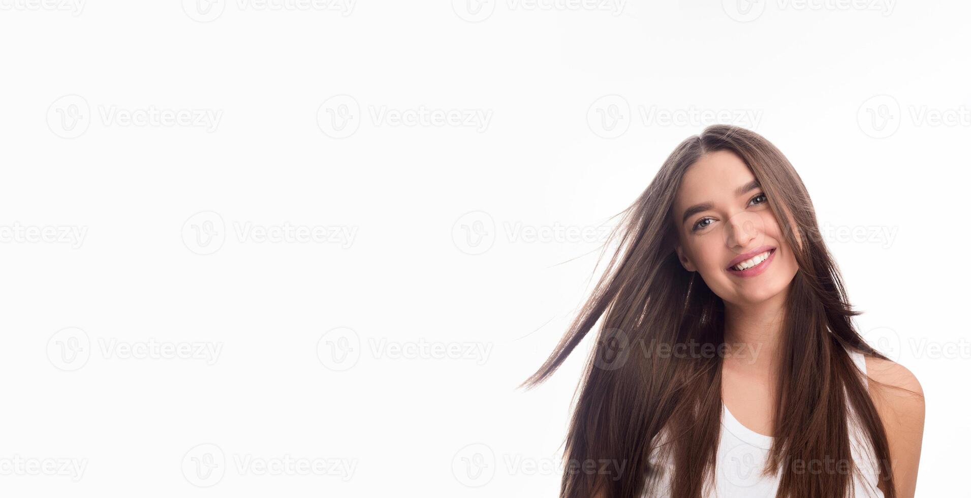 A young woman with long hair is smiling while standing in front of a white background. She exudes happiness and confidence as she poses for the camera. photo