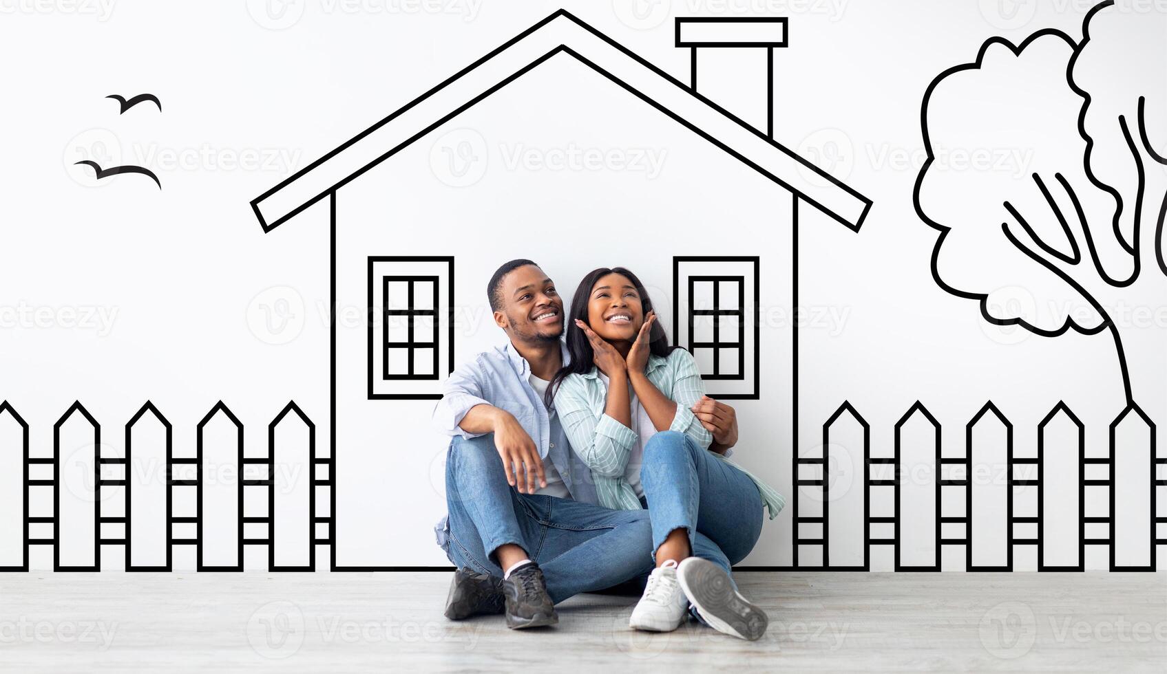 Cute black family husband and wife sitting over drawn on white wall house, embracing and smiling. Real estate, mortgage concept photo