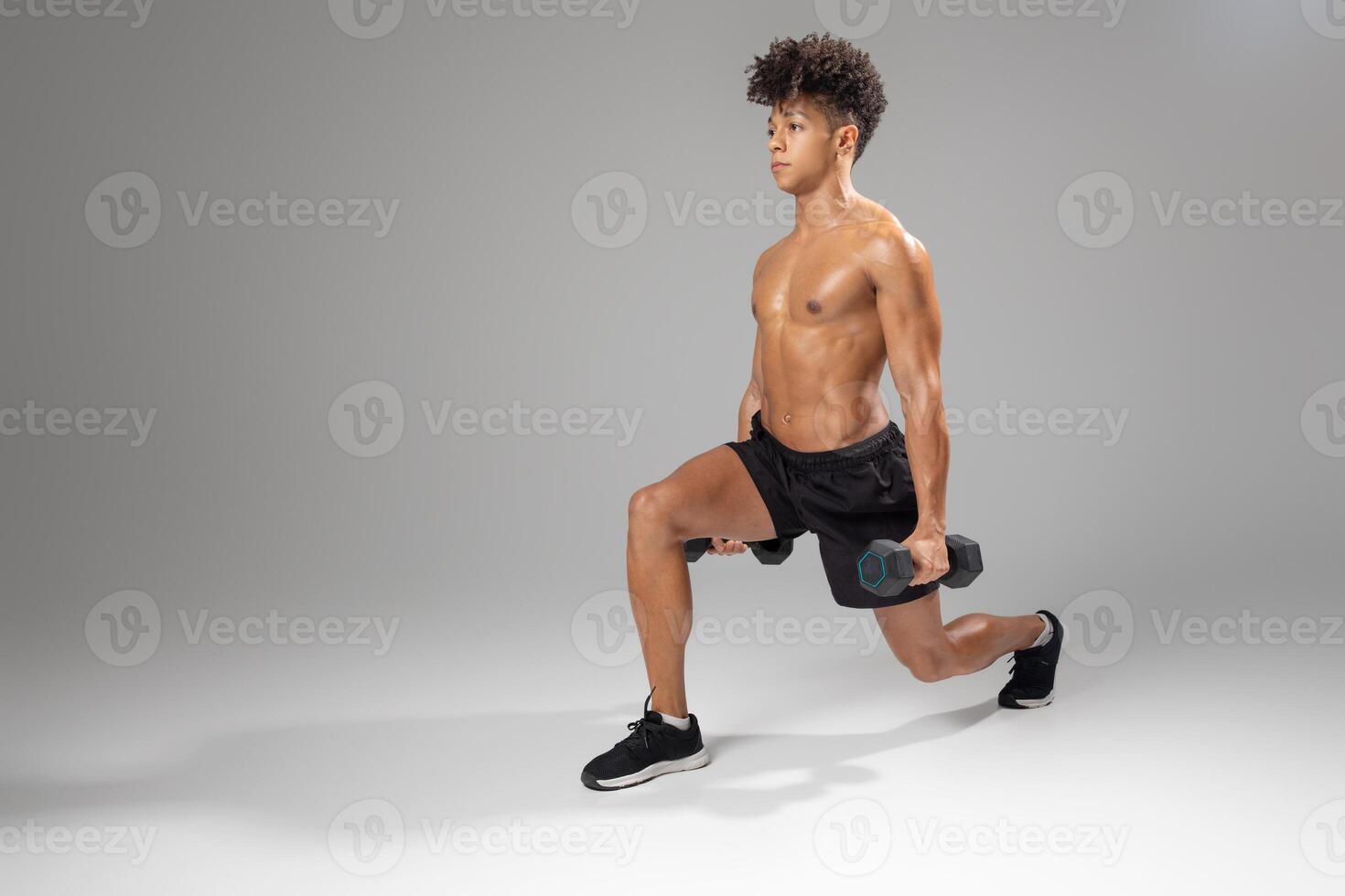 A young man is performing a lunge exercise while holding dumbbells in each hand. He is focused and maintains proper form during his workout session, copy space photo