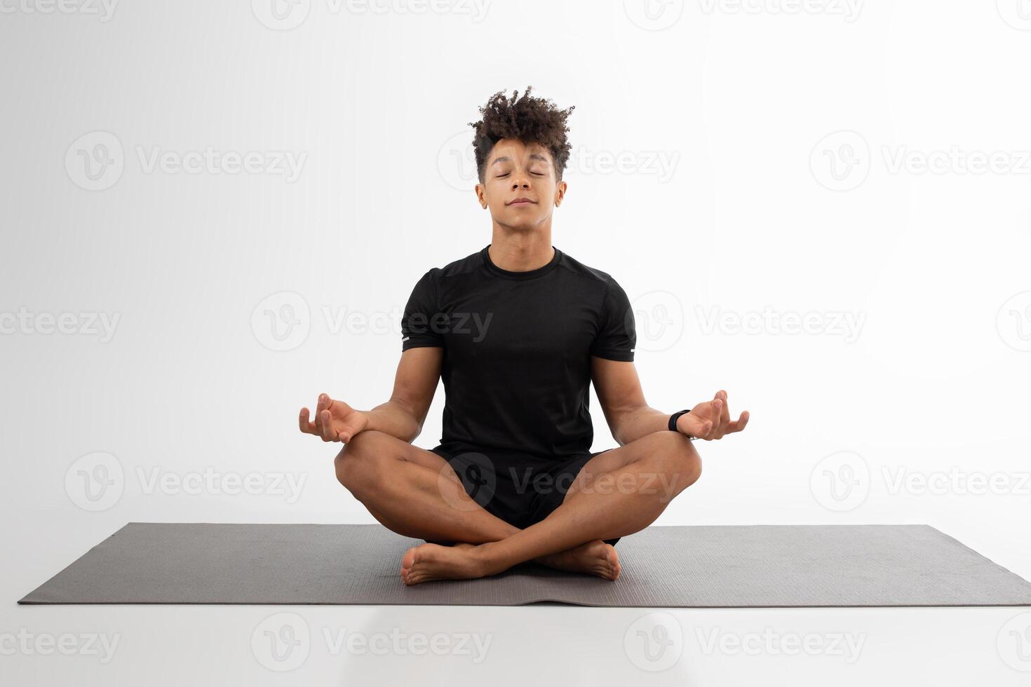 A man sits cross-legged on a yoga mat, eyes closed, in a state of deep concentration and tranquility. The spacious indoor setting highlights the calming atmosphere, encouraging mindfulness photo