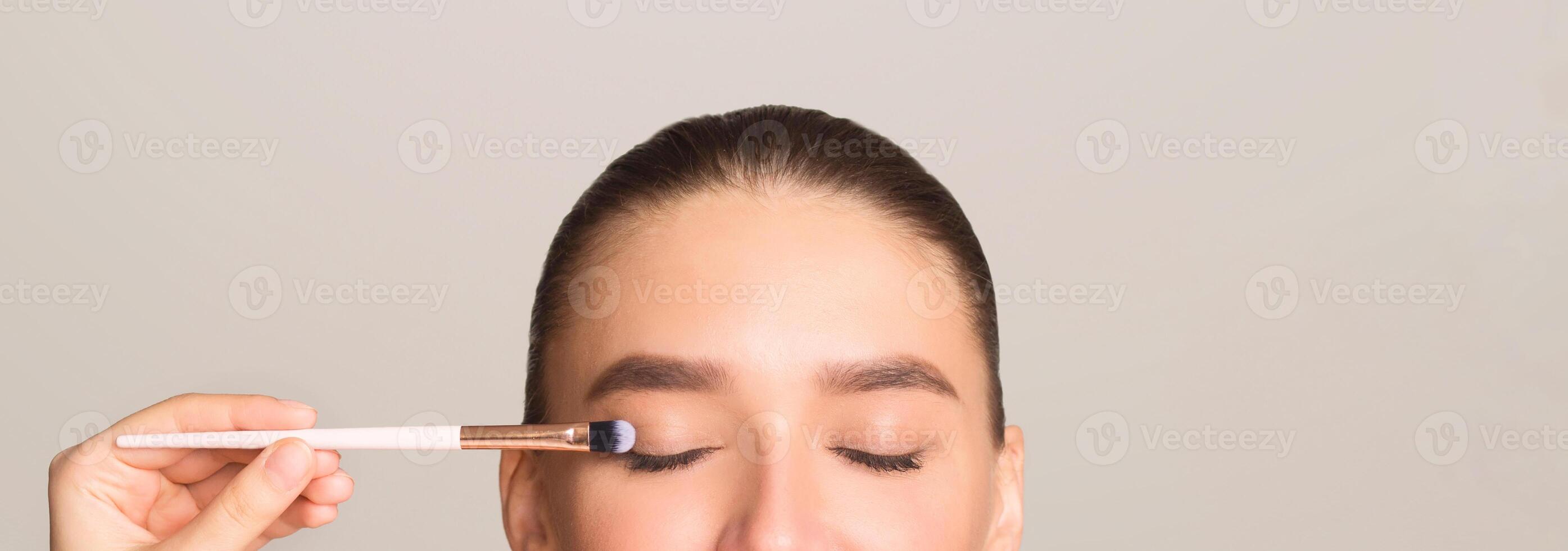 A woman is using a brush to apply makeup on her eyes. She is carefully brushing each eyelids to achieve a well-defined and neat look. photo