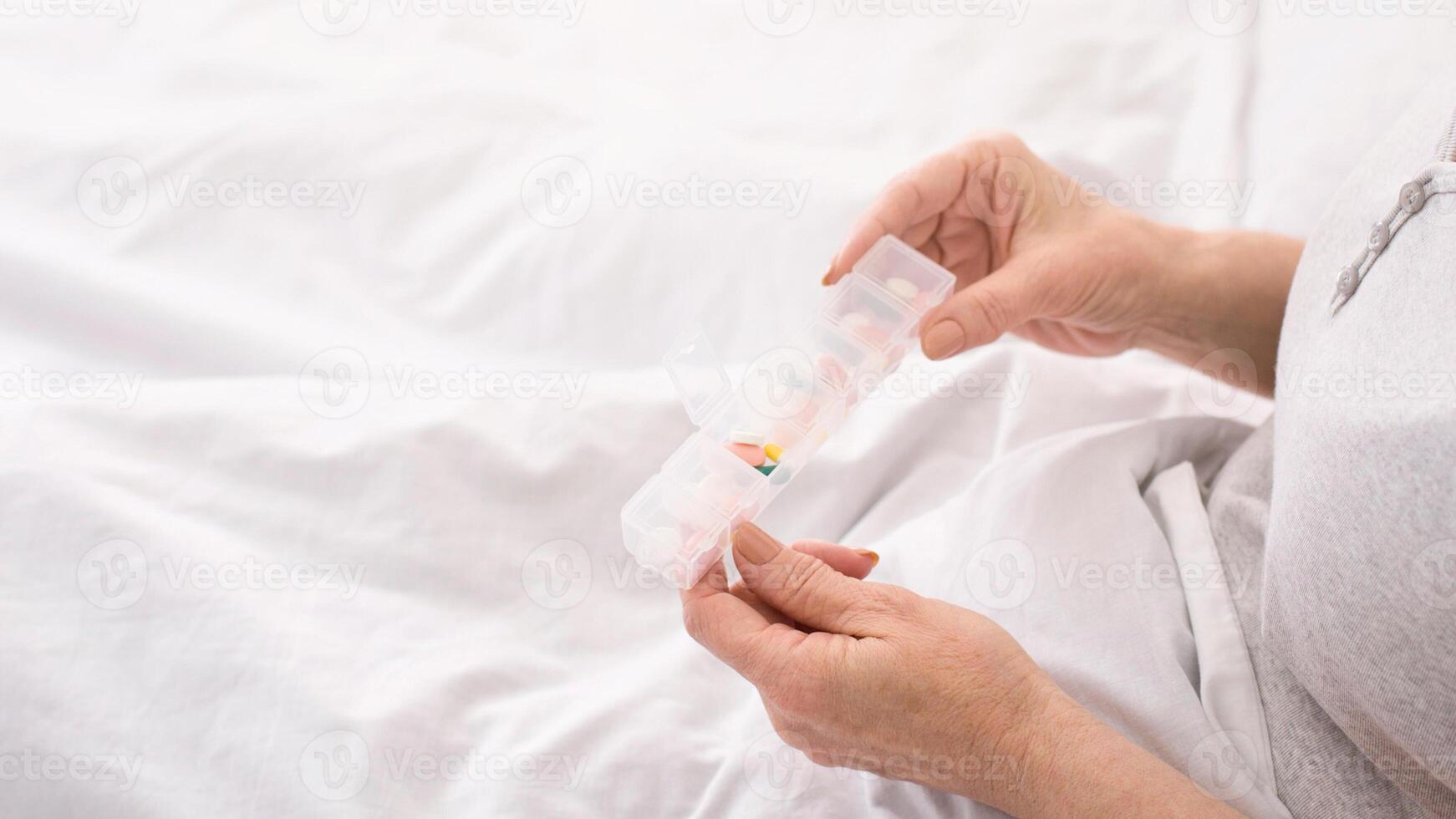 Cropped of an elderly woman hands as she carefully places various pills and capsules into a daily pill organizer, ensuring proper medication management from the comfort of her bedroom. photo