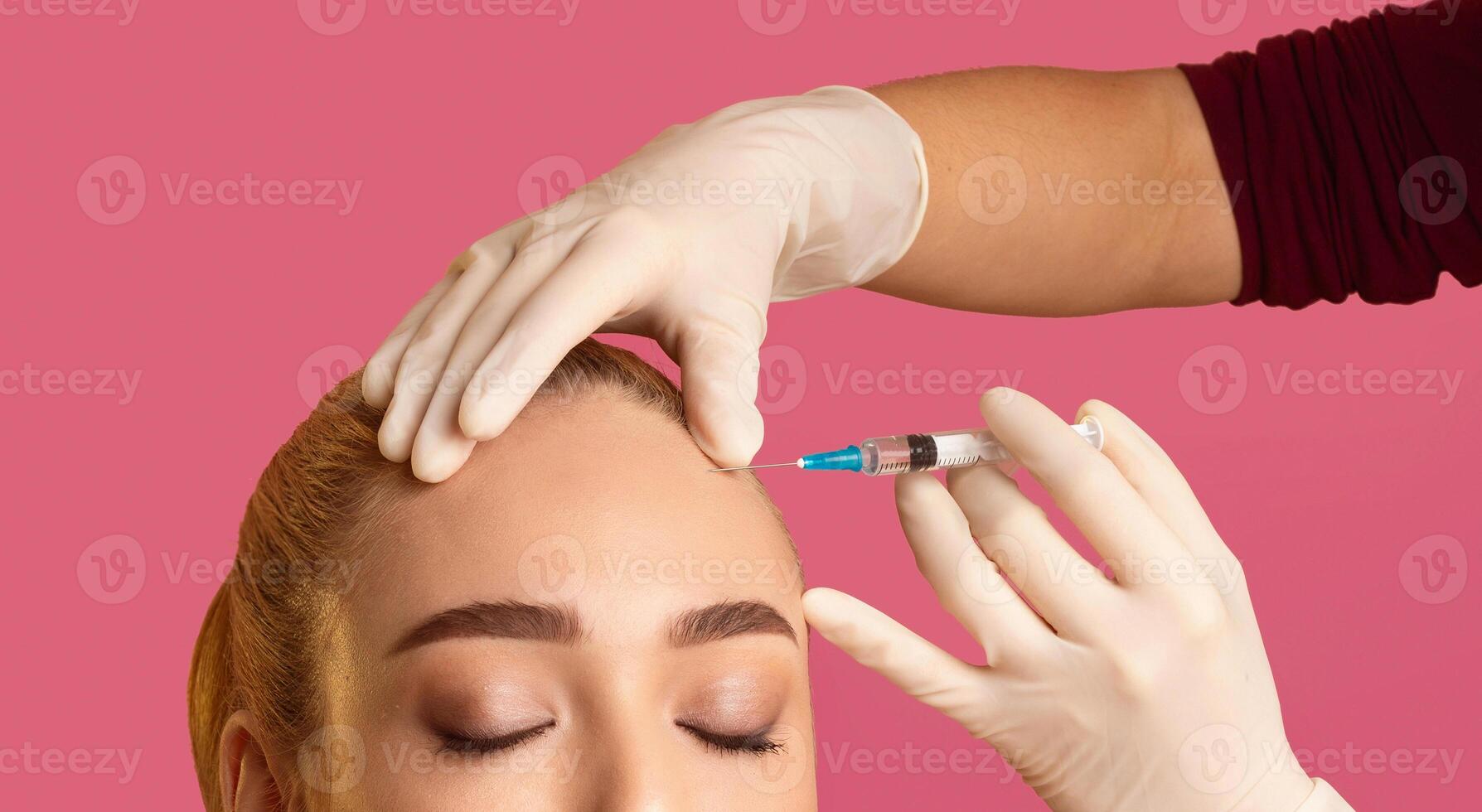 A close-up image of a woman receiving an injection in her forehead from a medical professional wearing white gloves. The woman has her eyes closed and is relaxed, with her hair pulled back photo