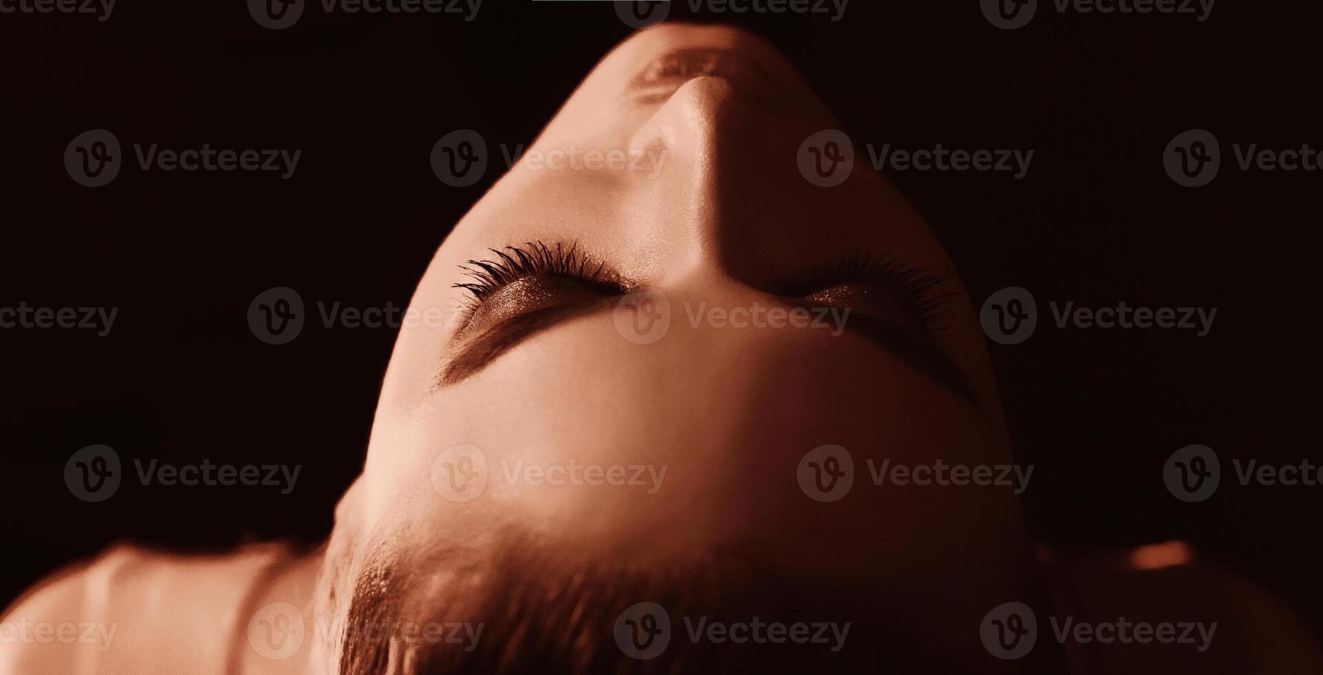 A young woman face is illuminated in the darkness, casting shadows and highlighting her features, closeup shot photo