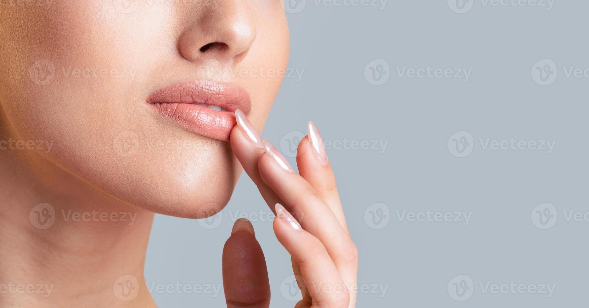 This image is a close-up of a woman lip, with her finger touching the bottom lip. The background is a light blue-gray, which emphasizes the woman lip and skin, cropped, copy space photo