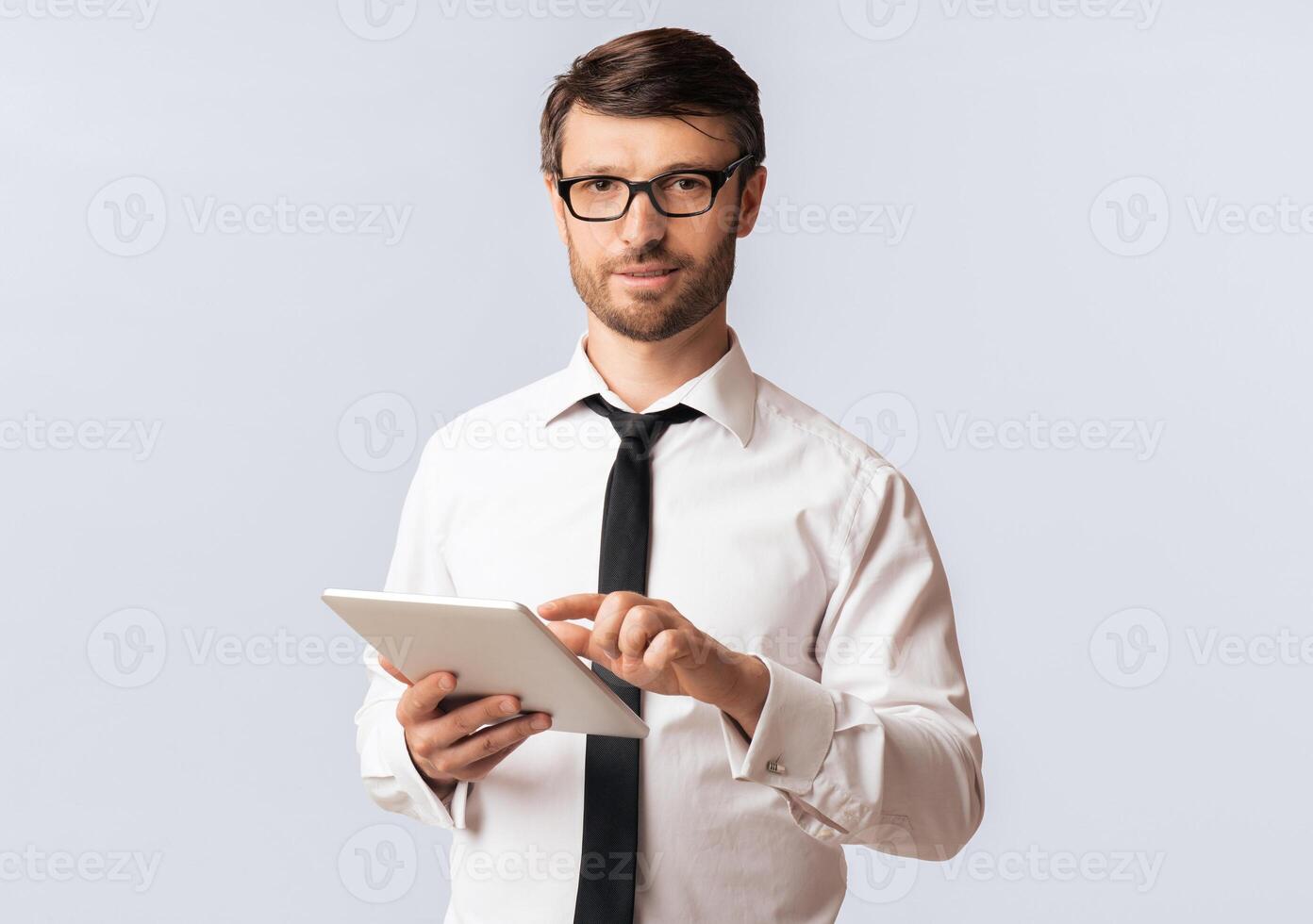 A man wearing a white shirt and tie uses a tablet while looking at the camera. photo