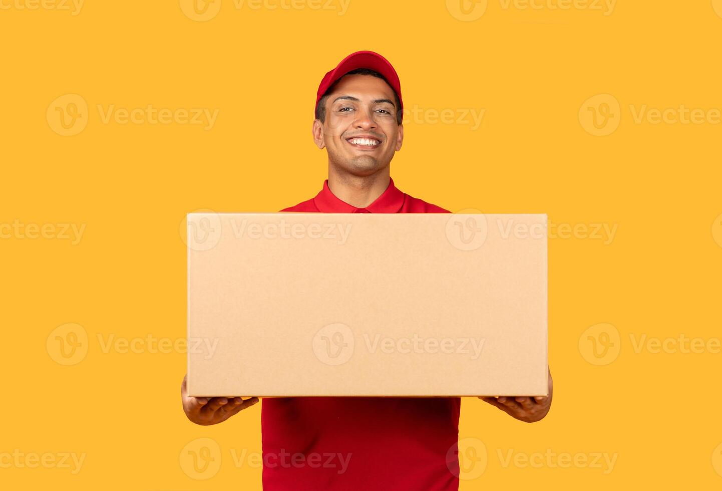 A man wearing a red shirt is seen grasping a cardboard box in his hands. The man appears to be standing upright, firmly holding onto the box with a focused expression on his face. photo