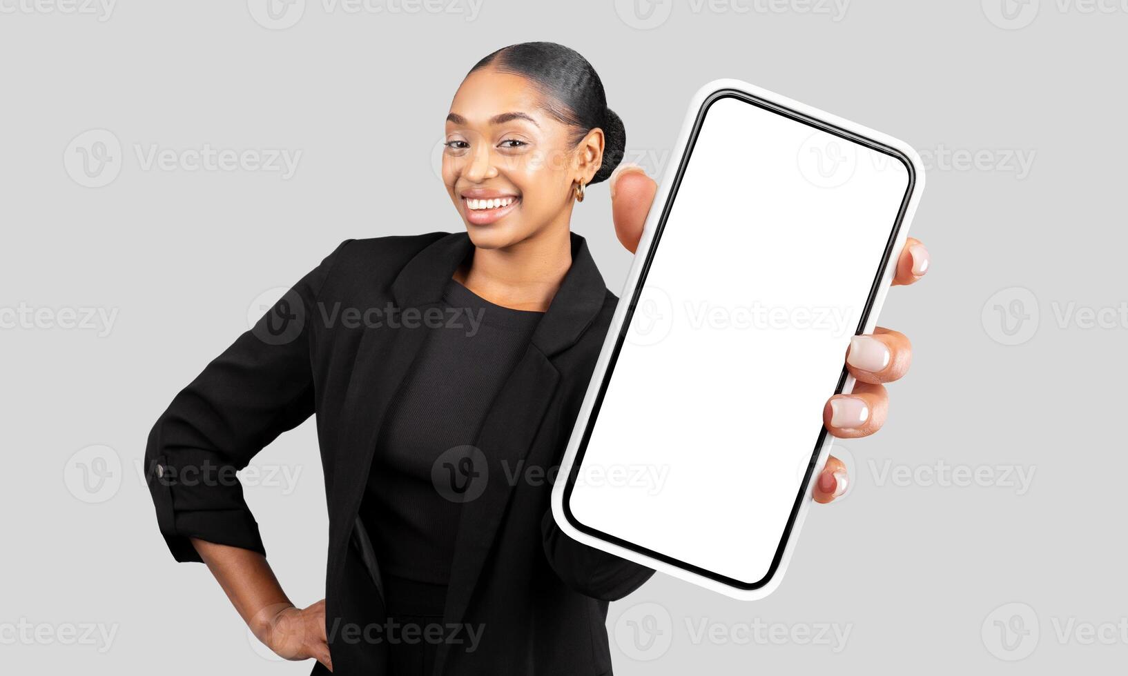 A smiling African American woman wearing a black blazer is holding a smartphone with a white screen. The smartphone is prominently displayed, with the woman face visible in the background photo