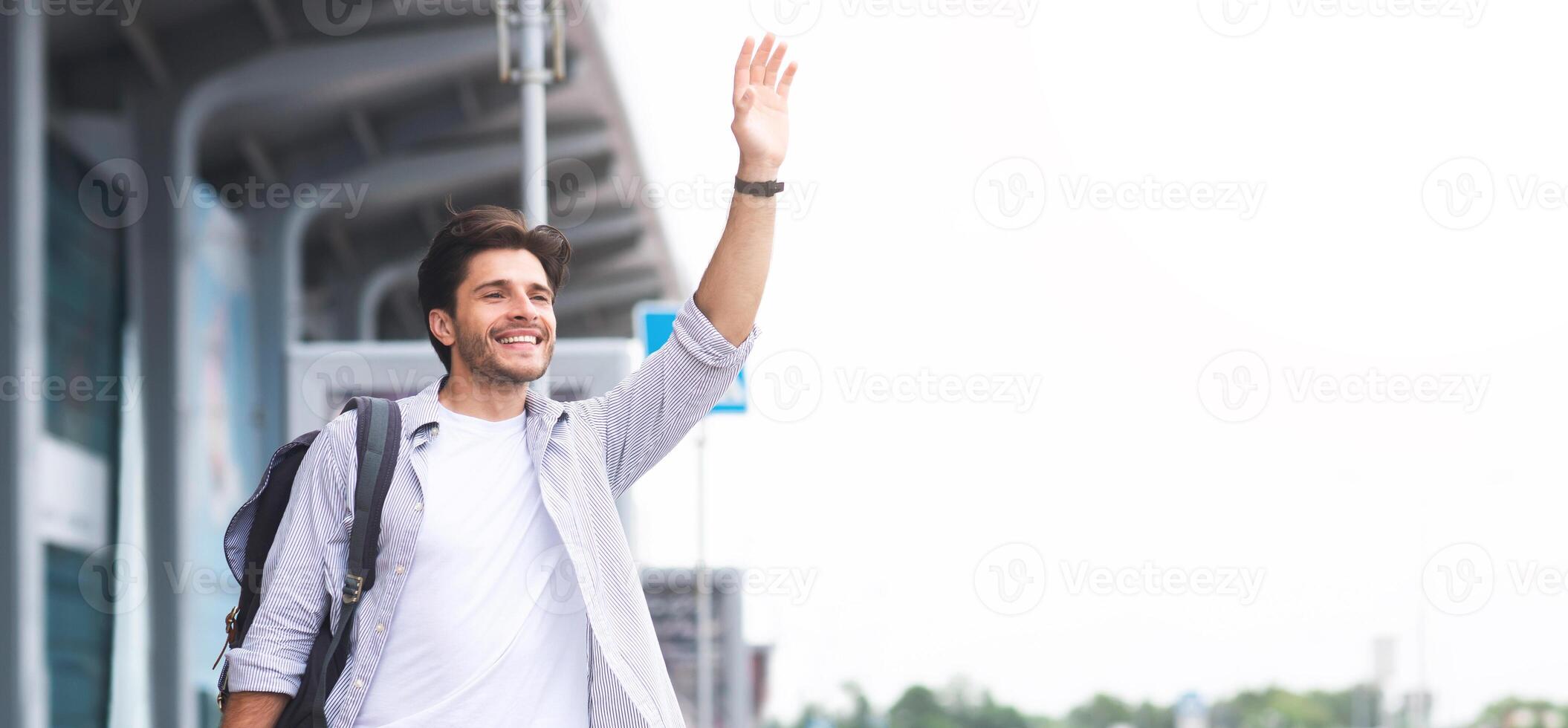 Catching a taxi. Young man waving hand near airport building, panorama with empty space photo