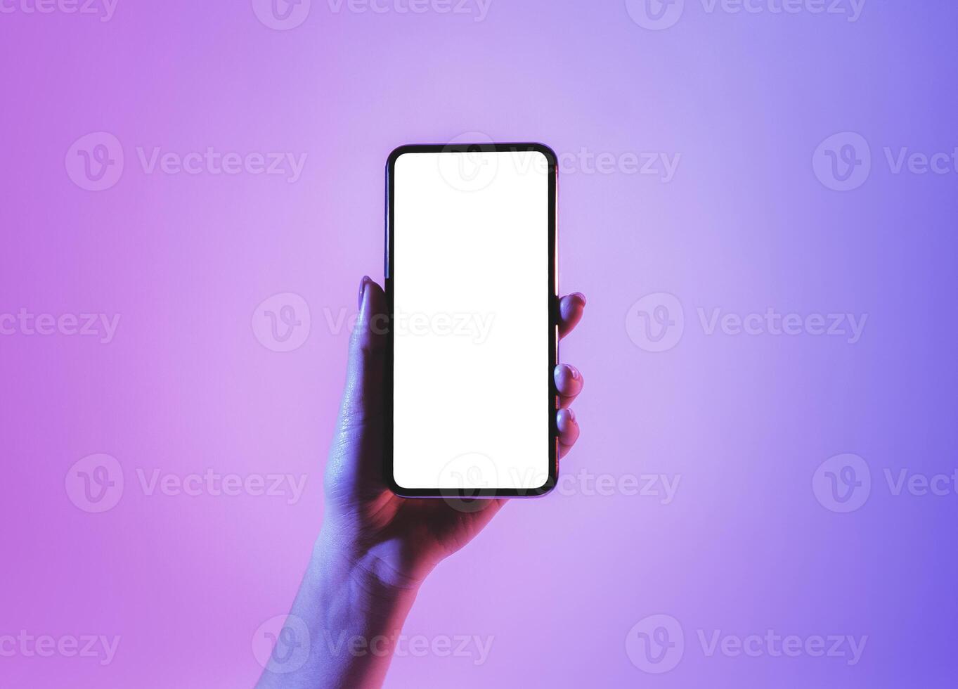 Hand holds smartphone with blank screen in neon, free space photo