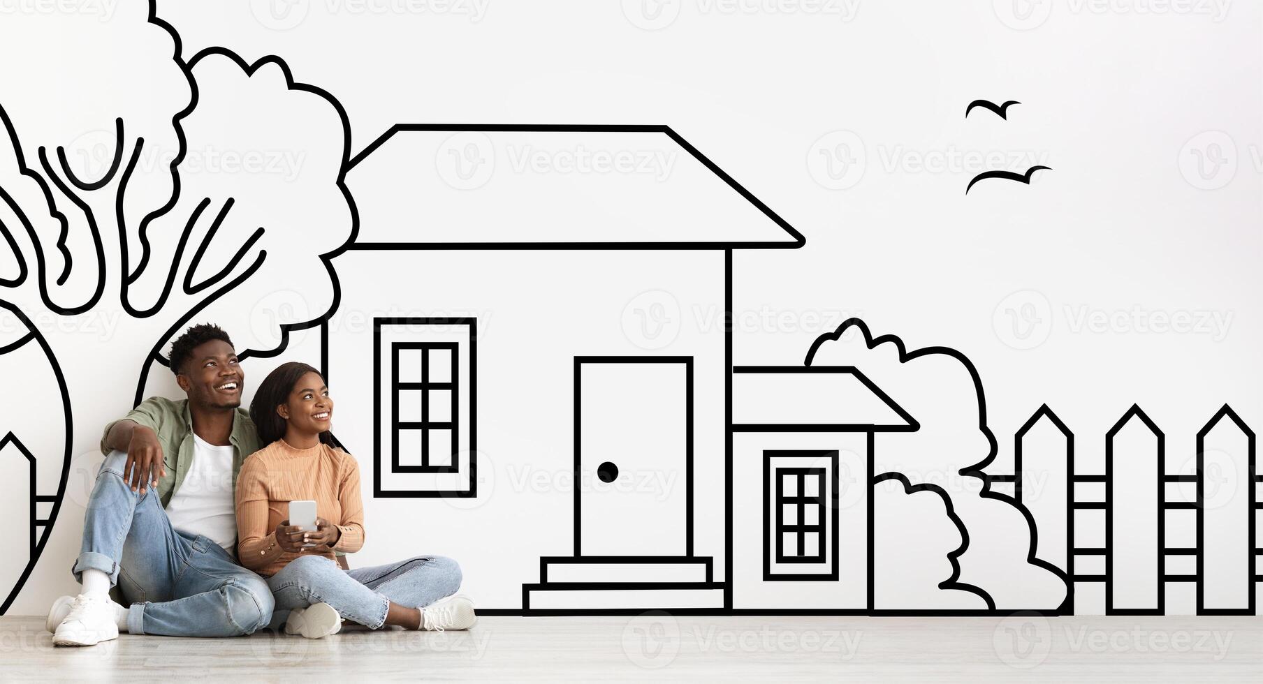 Black man and woman spouses are sitting on the floor, facing a detailed drawing of a house. They appear engaged in conversation, possibly discussing the architecture or design of the house. photo