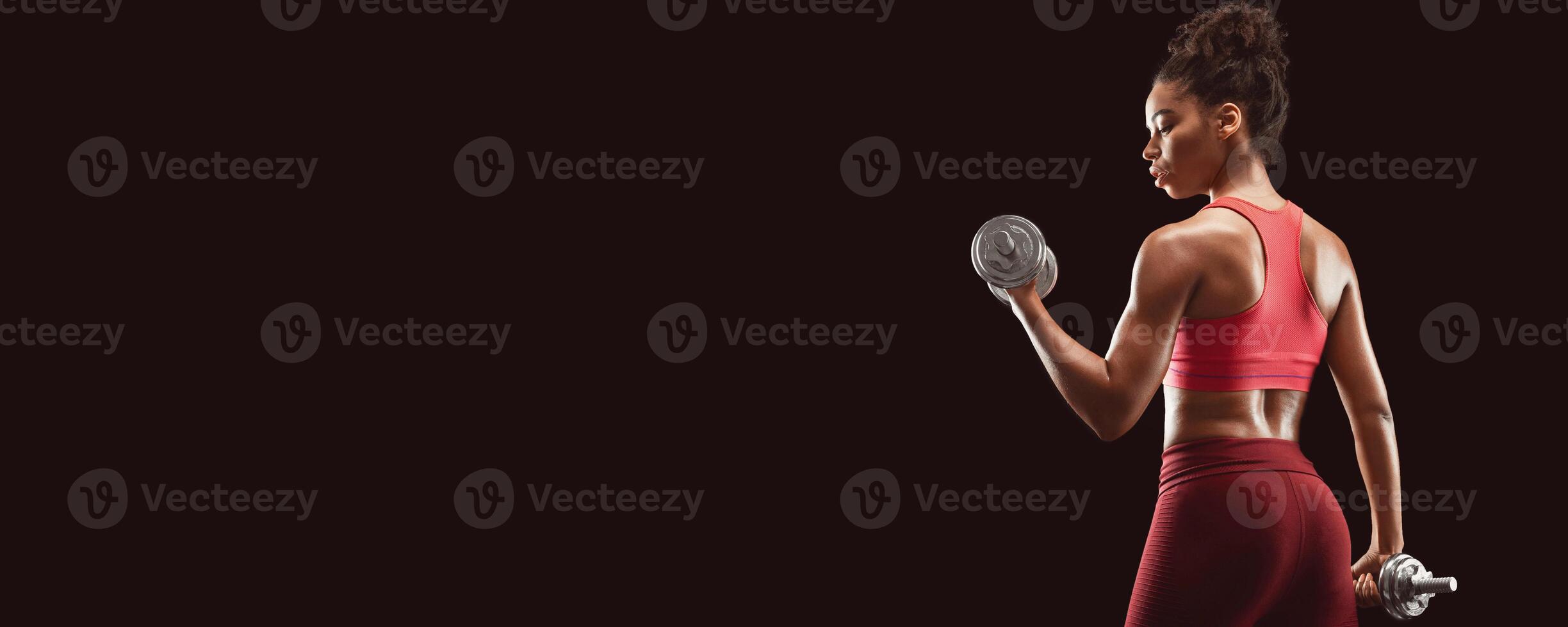 Black fitness lady doing workout with dumbbells, back view, black studio background, panorama with copy space photo