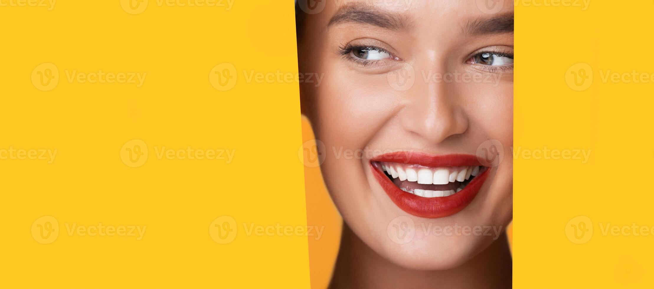 A woman face is partially visible through a round hole in a bright yellow background. She appears to be looking directly at copy space, with a neutral expression, panorama photo
