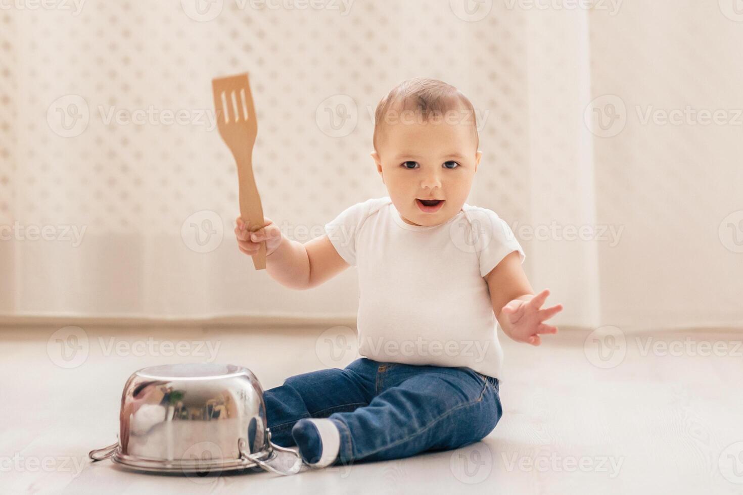 A small baby is seated on the floor, gripping a spatula in their tiny hands. The infant seems curious and engaged as they explore the kitchen utensil. photo