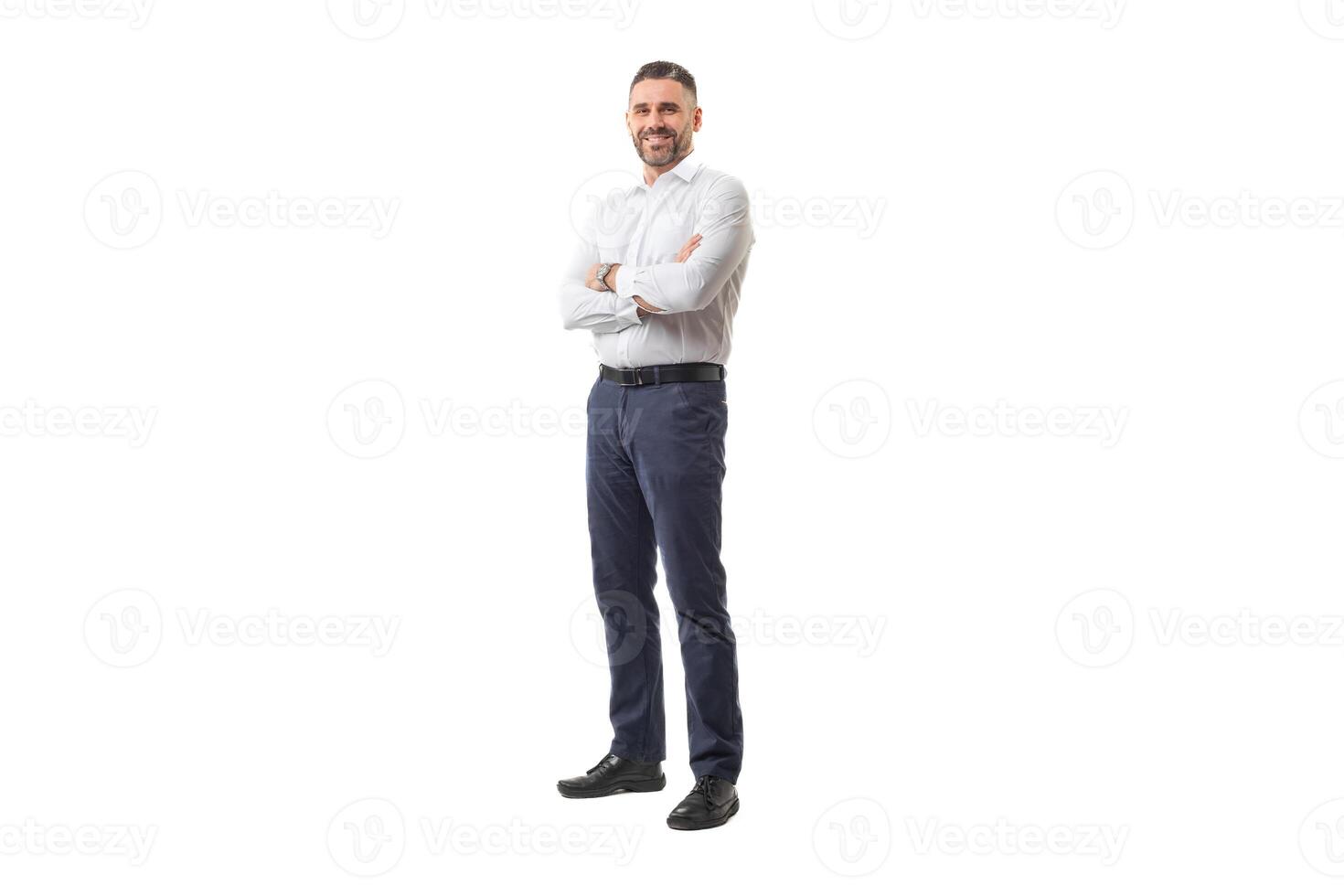 A confident businessman is standing with his arms crossed, wearing a white shirt and blue pants. He appears to be in a studio setting during daytime, smiling and exuding confidence. photo