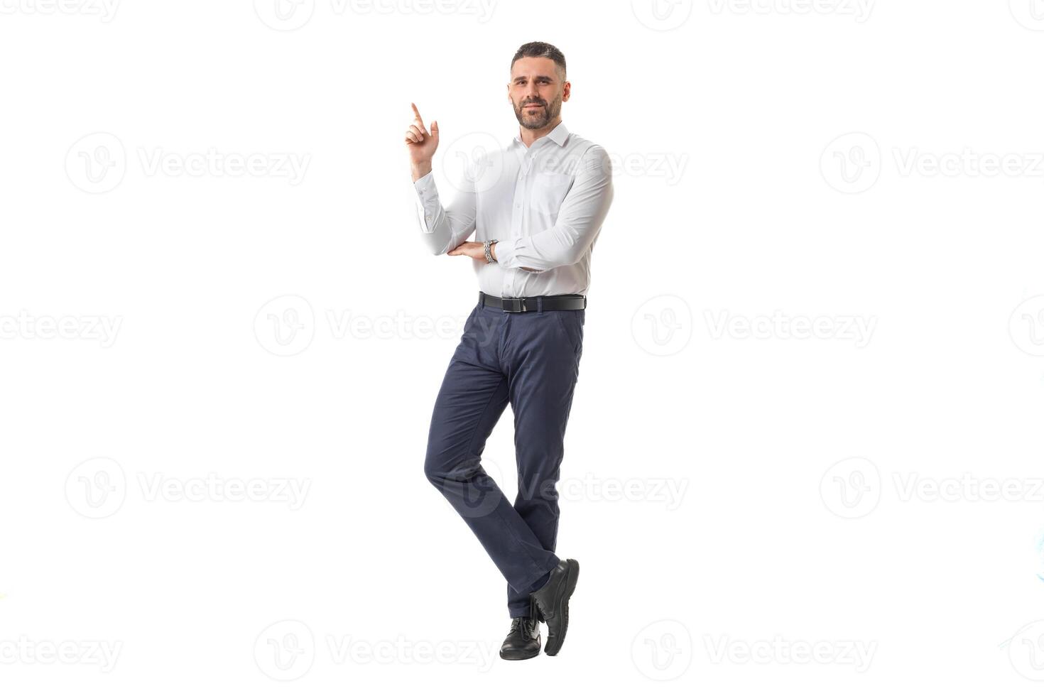 A man dressed in a white shirt and black pants poses confidently, pointing upwards with his finger, suggesting an idea or giving advice. photo