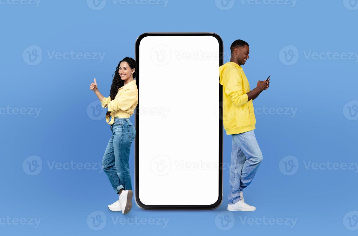 Energetically, the young multiracial couple engages with viewers, standing next to a mockup smartphone that offers a clear, unoccupied screen for various displays. photo